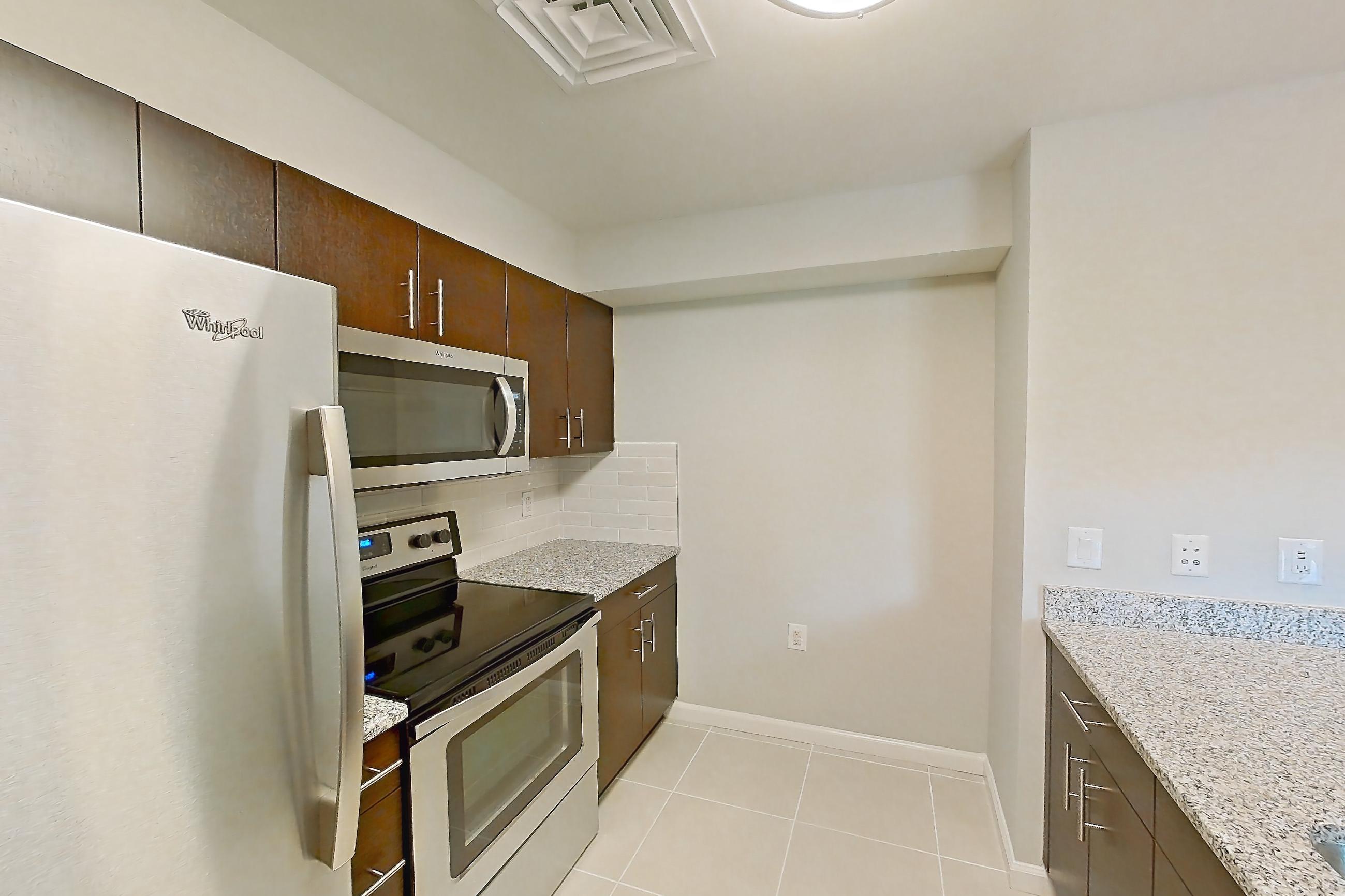 Kitchen with dishwasher, electric range, light countertops, light stone countertops, light tile flooring, light wood-finish flooring, microwave, oven/range, refrigerator, stainless steel appliances, and white appliances, Apartment RT-0615 at RiverTrace at Port Imperial