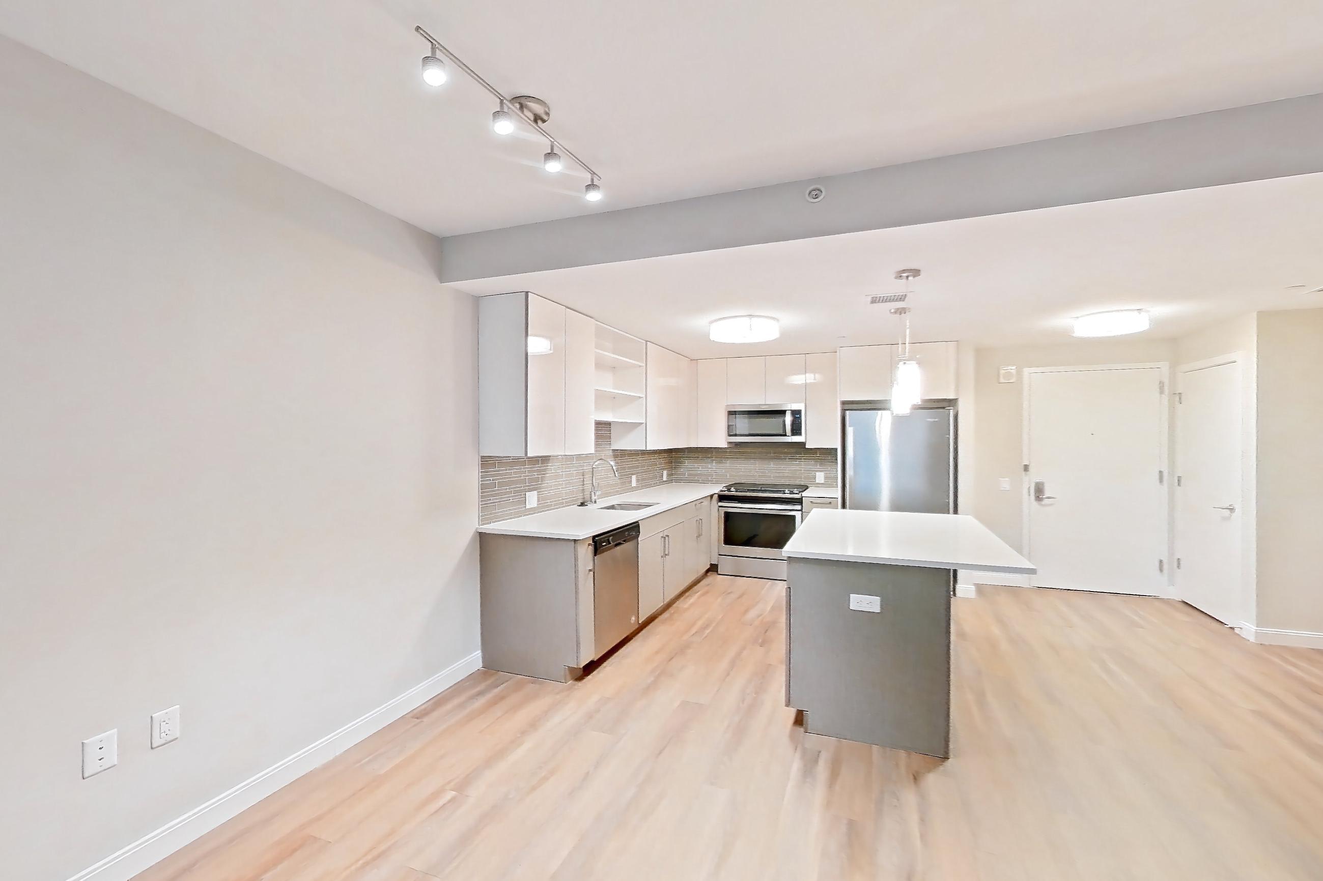 Living room with dark wood-finish flooring, dishwasher, light countertops, light wood-finish flooring, oven/range, refrigerator, and stainless steel appliances, Apartment RH-0437 at RiverHouse11