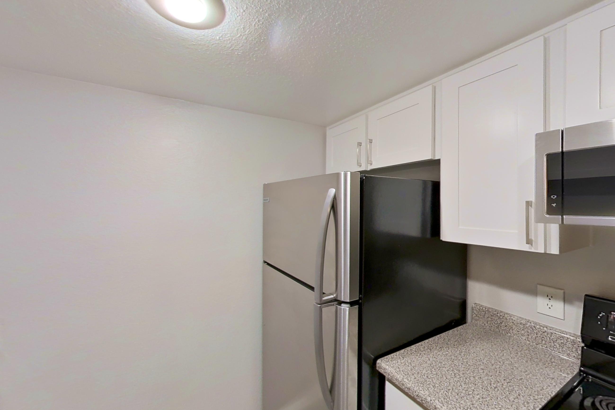 Kitchen with black appliances, dishwasher, electric range, light stone countertops, light wood-finish flooring, oven/range, refrigerator, and stainless steel appliances, Apartment 18 at Avana Rancho Cucamonga