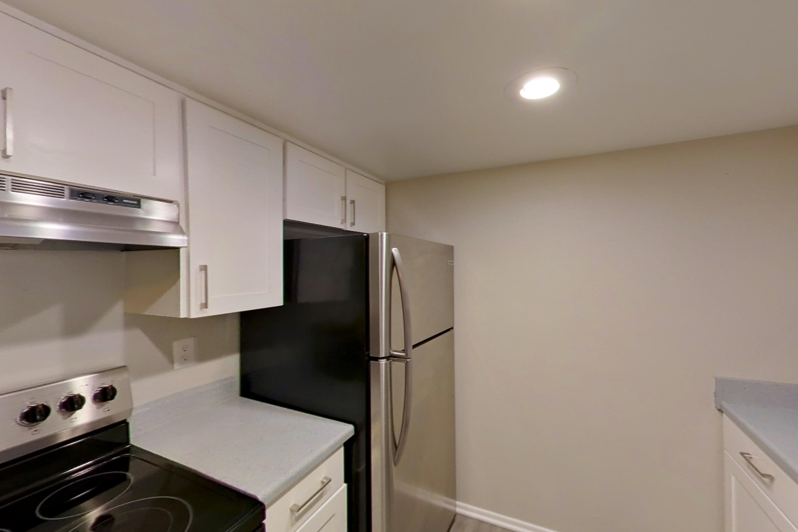 Kitchen with electric range, light countertops, light stone countertops, light wood-finish flooring, oven/range, range hood, refrigerator, and stainless steel appliances, Apartment 05 at Avana Rancho Cucamonga
