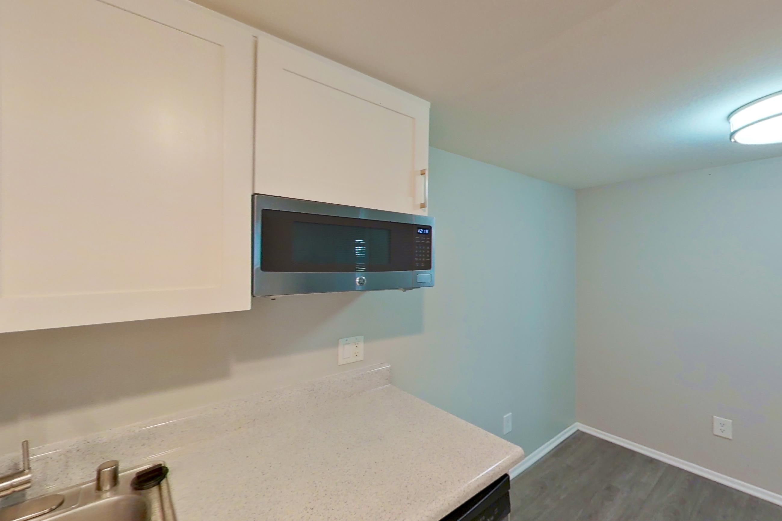 Kitchen with dishwasher, electric range, light countertops, light stone countertops, light vinyl flooring, light wood-finish flooring, oven/range, range hood, refrigerator, stainless steel appliances, and white appliances, Apartment 12 at Avana Rancho Cucamonga