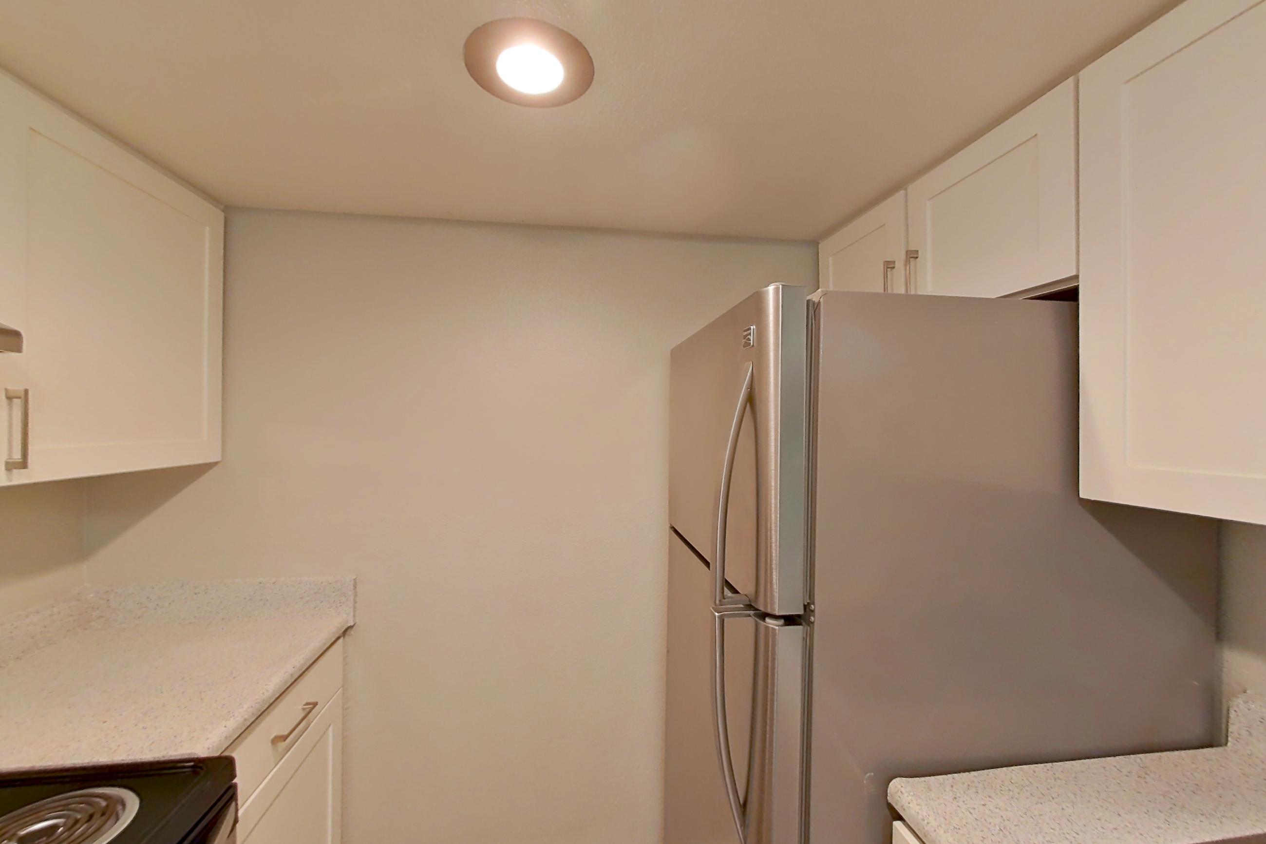 Kitchen with dishwasher, electric range, light countertops, light stone countertops, light vinyl flooring, light wood-finish flooring, oven/range, range hood, refrigerator, stainless steel appliances, and white appliances, Apartment 12 at Avana Rancho Cucamonga