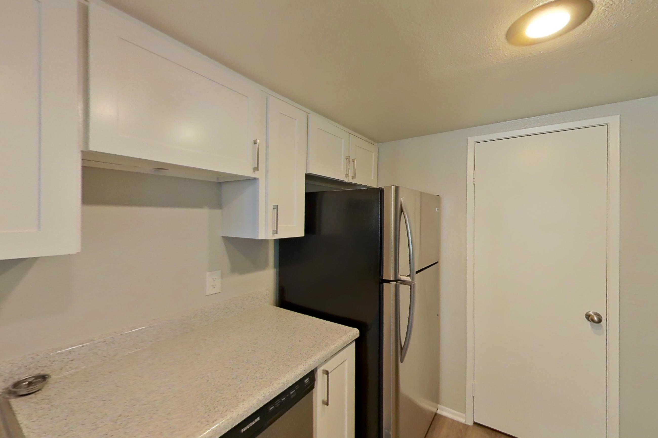 Kitchen with dishwasher, electric range, light countertops, light stone countertops, light wood-finish flooring, microwave, oven/range, refrigerator, and stainless steel appliances, Apartment 06 at Avana Rancho Cucamonga