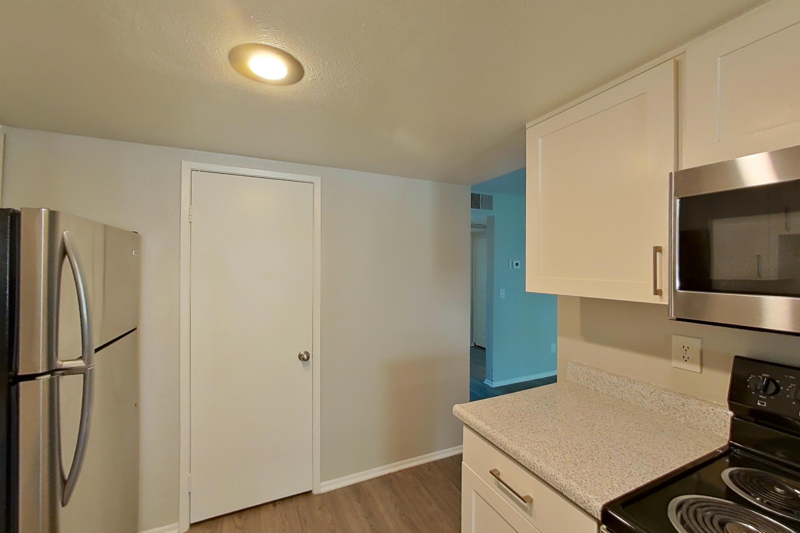 Kitchen with dishwasher, electric range, light countertops, light stone countertops, light wood-finish flooring, microwave, oven/range, refrigerator, and stainless steel appliances, Apartment 06 at Avana Rancho Cucamonga