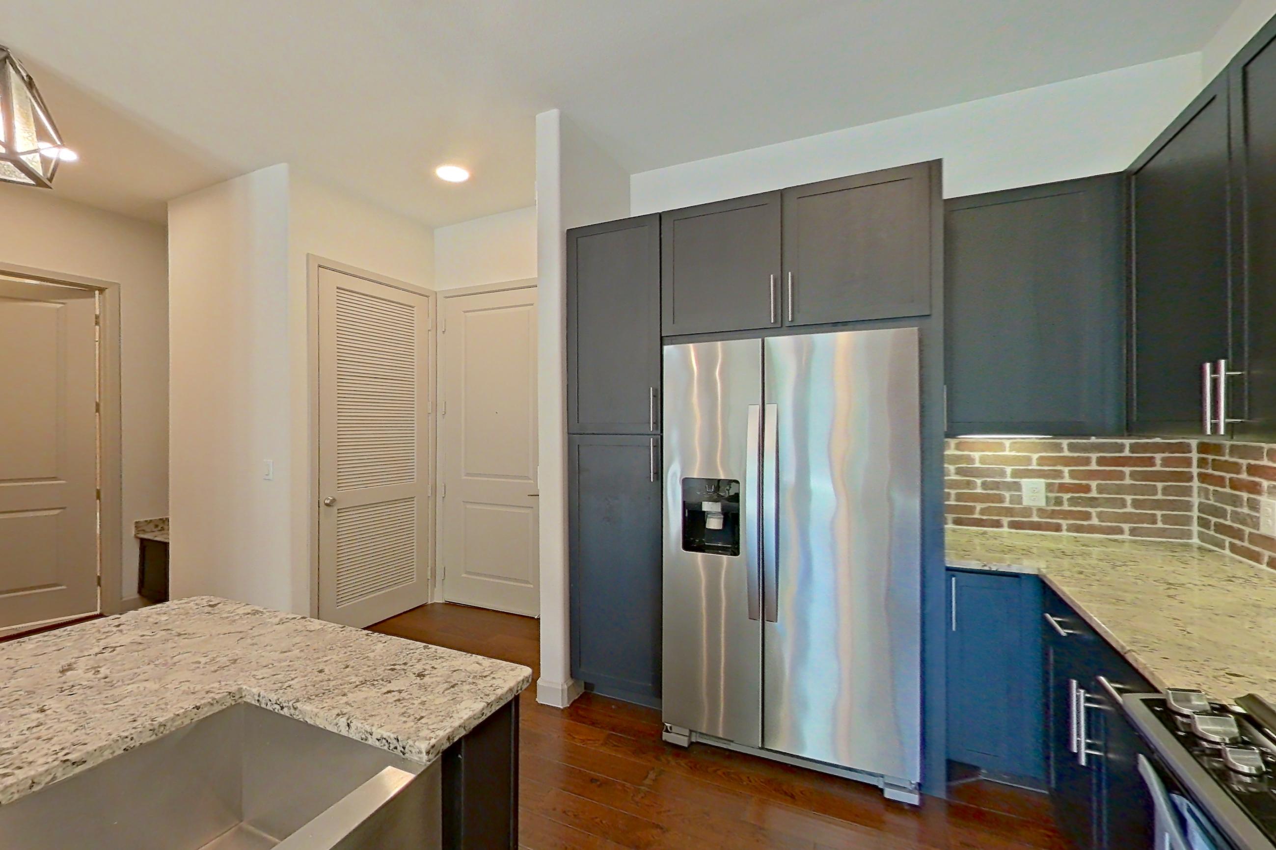 Kitchen with dark wood-finish flooring, dishwasher, gas range, light stone countertops, oven/range, refrigerator, stainless steel appliances, water & ice dispenser, and wood-finish flooring, Apartment 139 at Sinclair