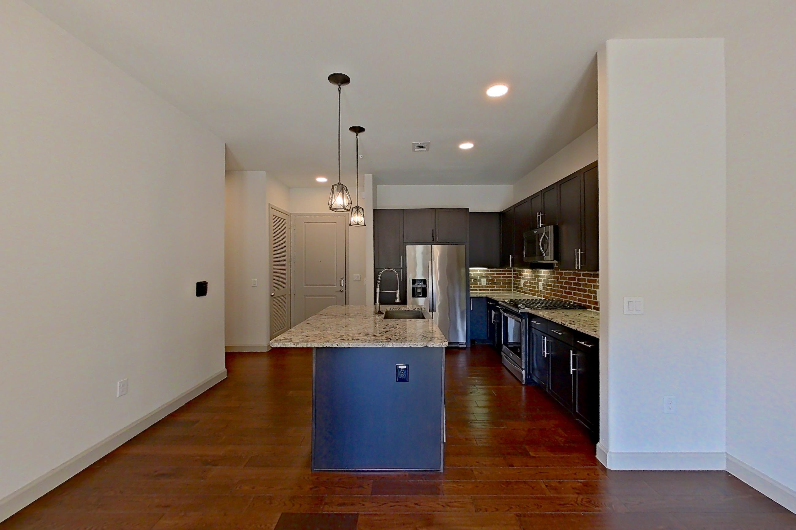 Living room with dark wood-finish flooring, gas range, kitchen island, light stone countertops, oven/range, refrigerator, stainless steel appliances, and water & ice dispenser, Apartment 139 at Sinclair