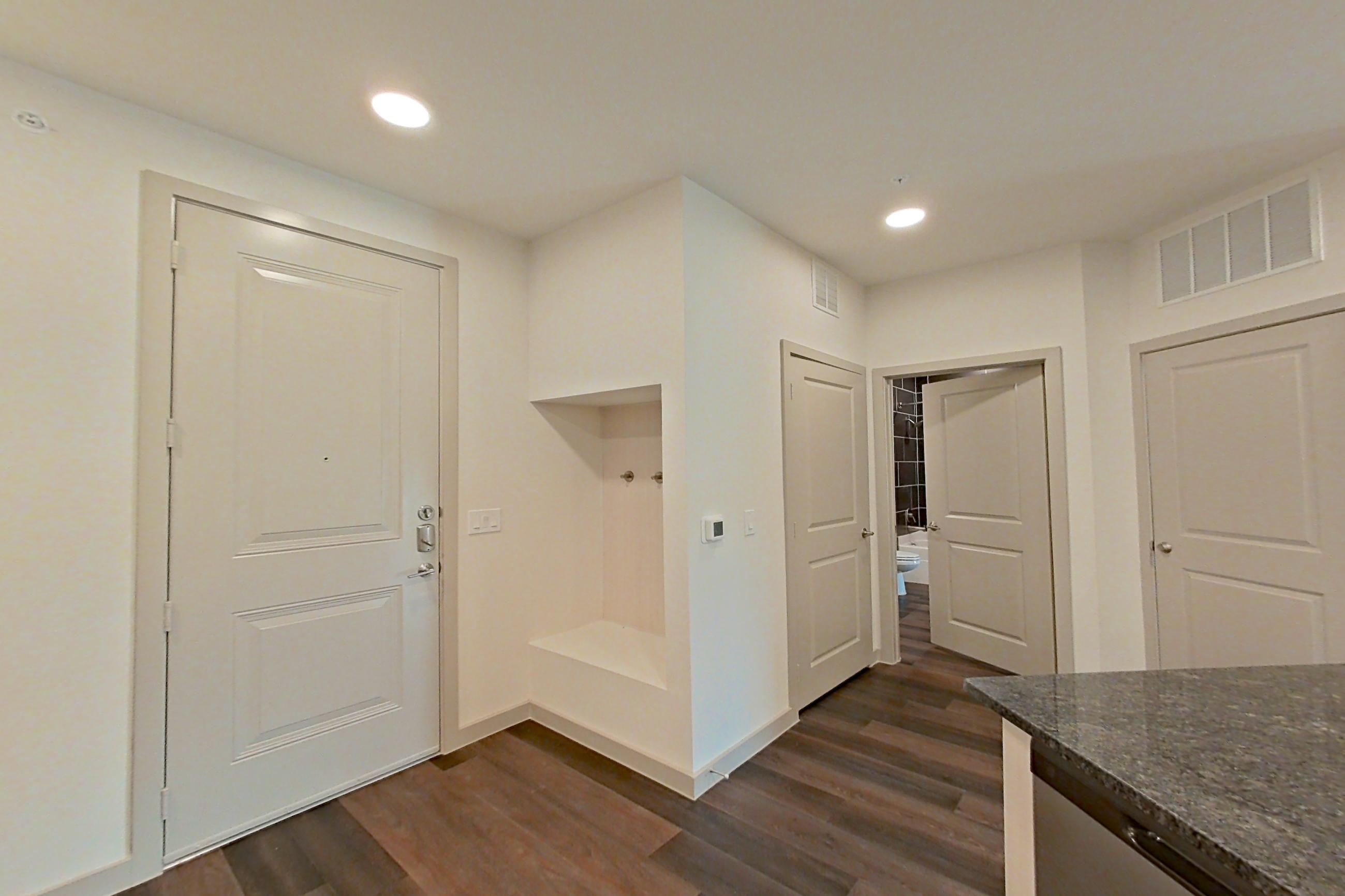 Kitchen with dark stone countertops, dark wood-finish flooring, dishwasher, electric range, light countertops, microwave, oven/range, refrigerator, stainless steel appliances, and water & ice dispenser, Apartment 1412 at Merit Lewisville