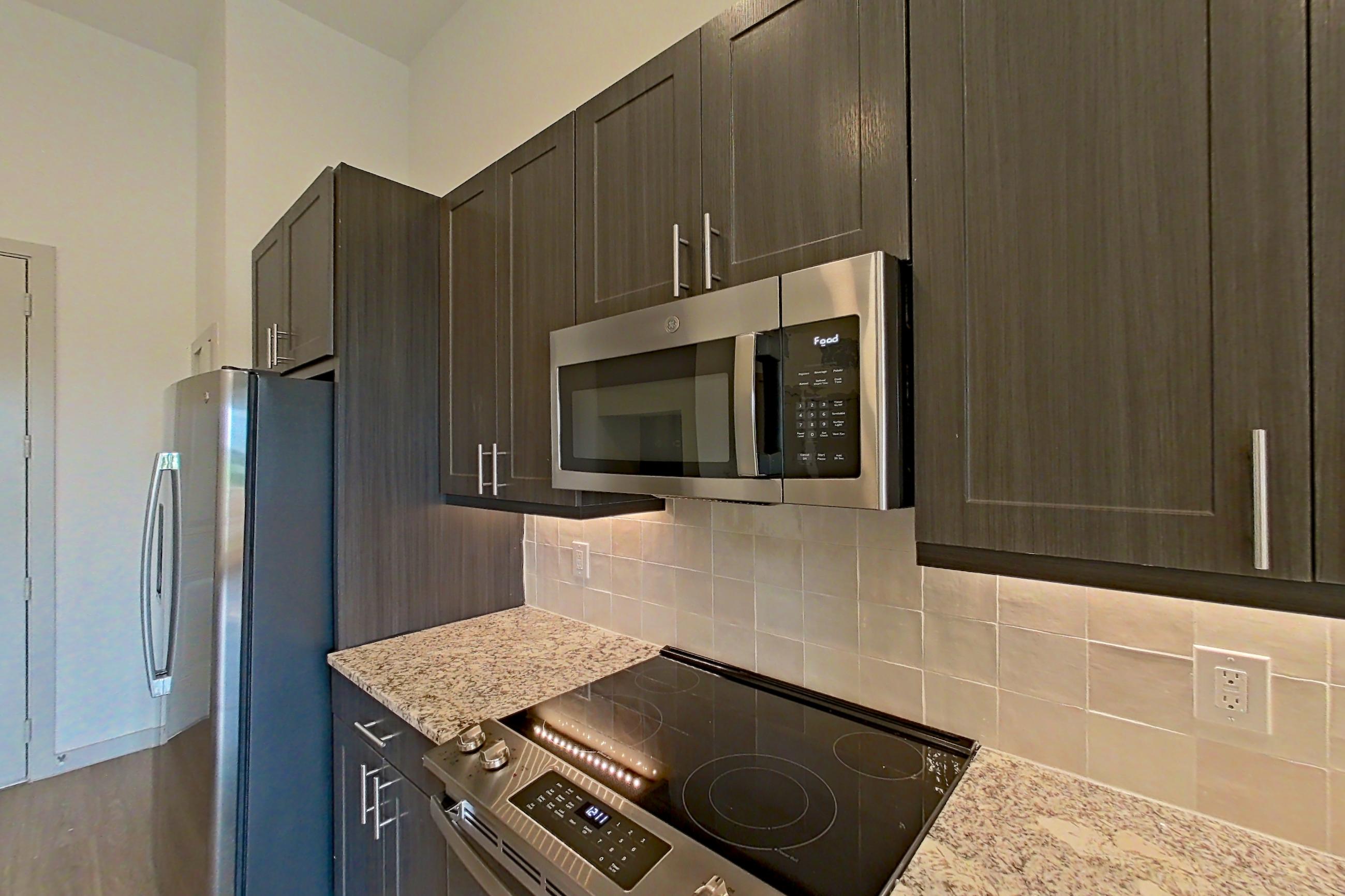 Kitchen with dishwasher, electric range, light stone countertops, light wood-finish flooring, microwave, oven/range, and stainless steel appliances, Apartment 2162 at Merit Lewisville