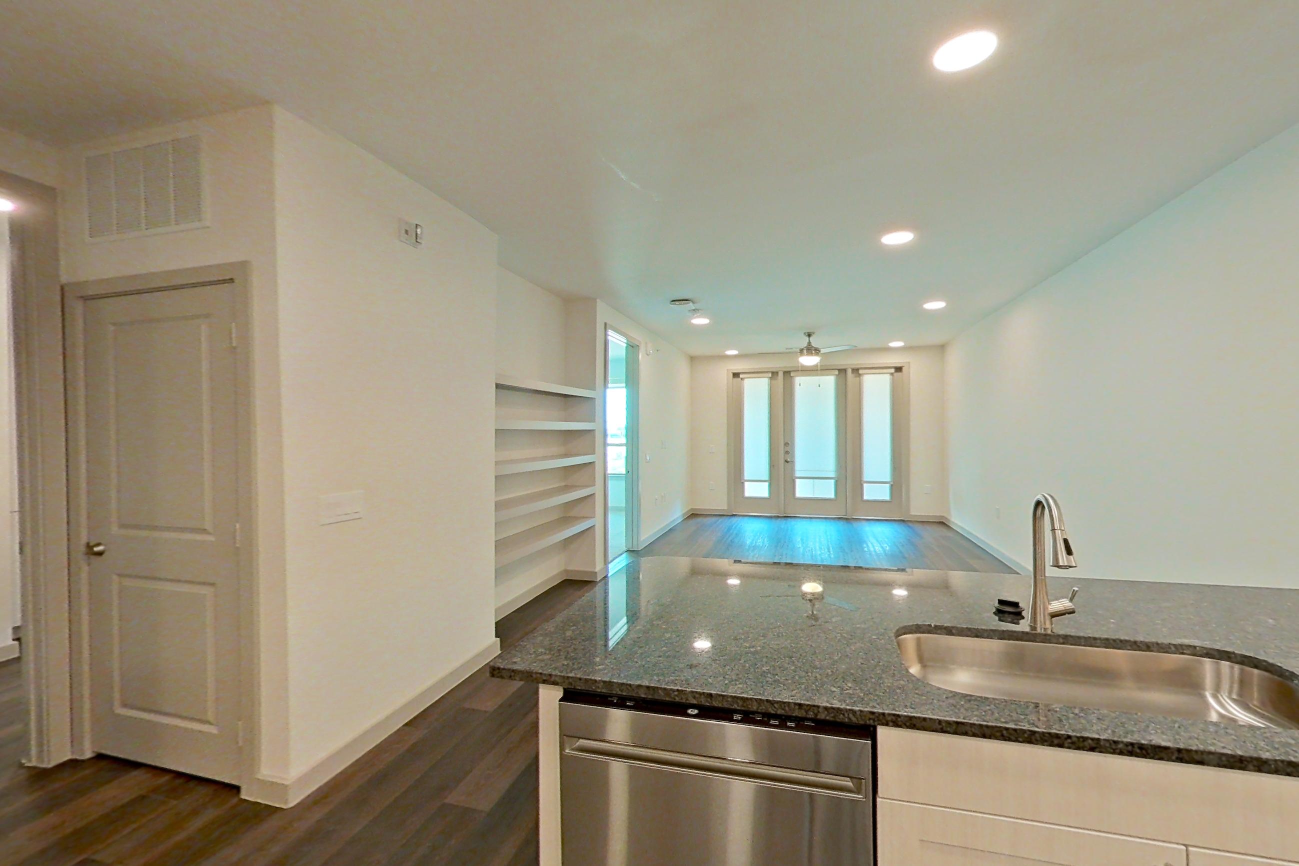 Kitchen with dark stone countertops, dark wood-finish flooring, dishwasher, electric range, oven/range, range hood, refrigerator, stainless steel appliances, and water & ice dispenser, Apartment 1208 at Merit Lewisville