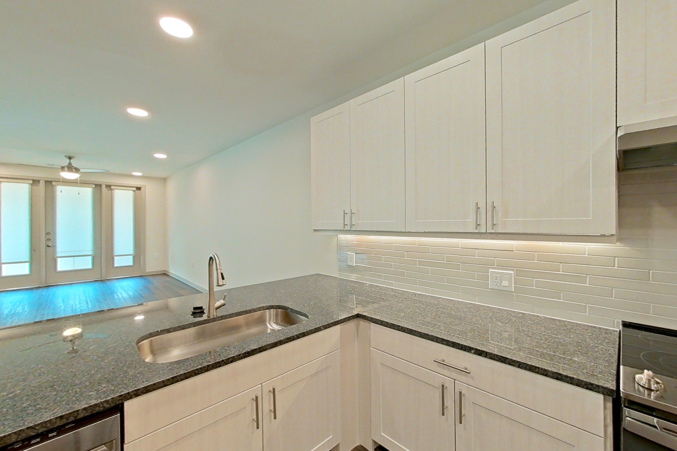 Kitchen with dark stone countertops, dark wood-finish flooring, dishwasher, electric range, oven/range, range hood, refrigerator, stainless steel appliances, and water & ice dispenser, Apartment 1208 at Merit Lewisville