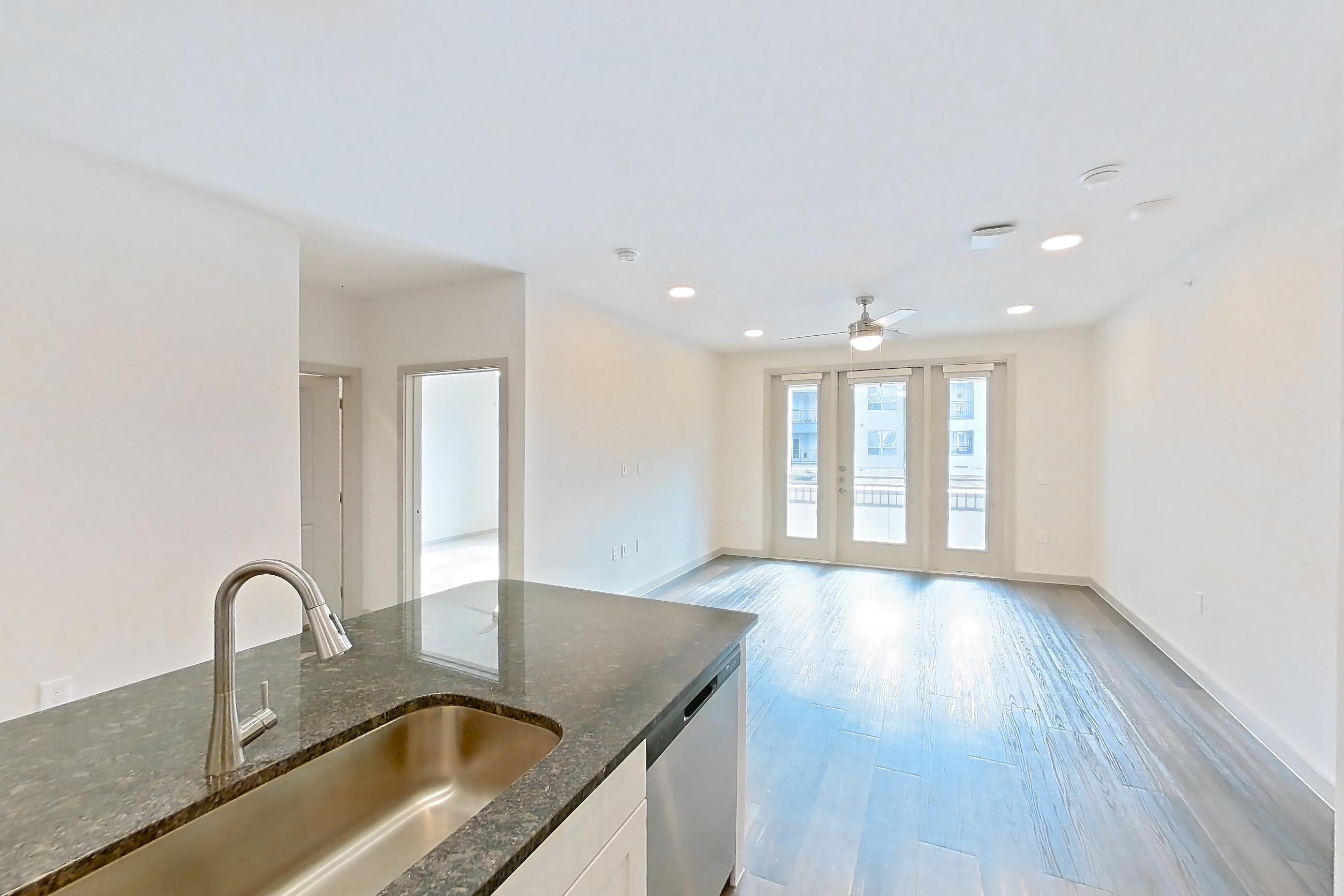 Kitchen with dark stone countertops, dark wood-finish flooring, dishwasher, electric range, microwave, oven/range, refrigerator, stainless steel appliances, and wood-finish flooring, Apartment 2230 at Merit Lewisville