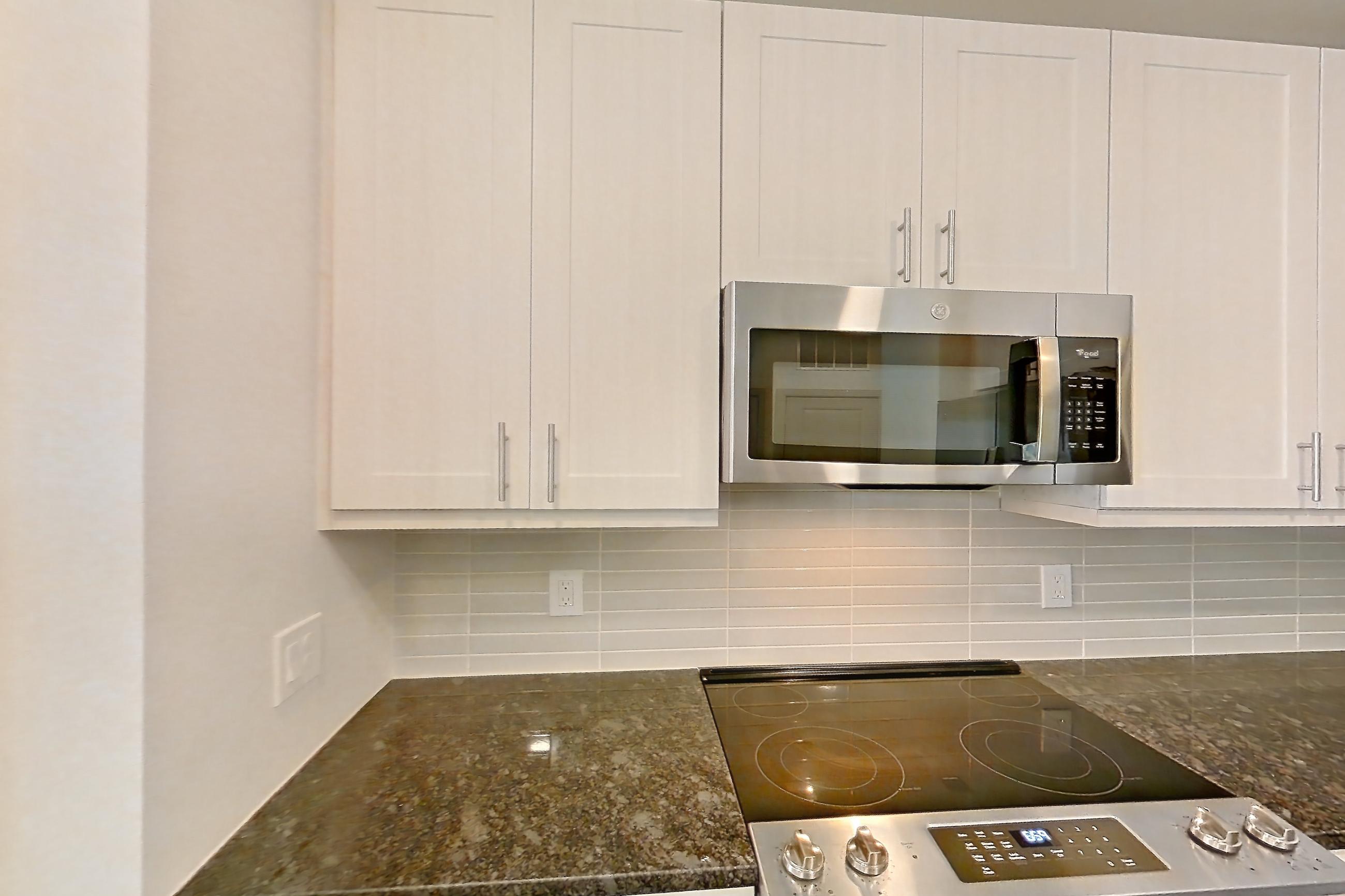 Kitchen with dark stone countertops, dark wood-finish flooring, dishwasher, electric range, microwave, oven/range, refrigerator, stainless steel appliances, and wood-finish flooring, Apartment 2230 at Merit Lewisville