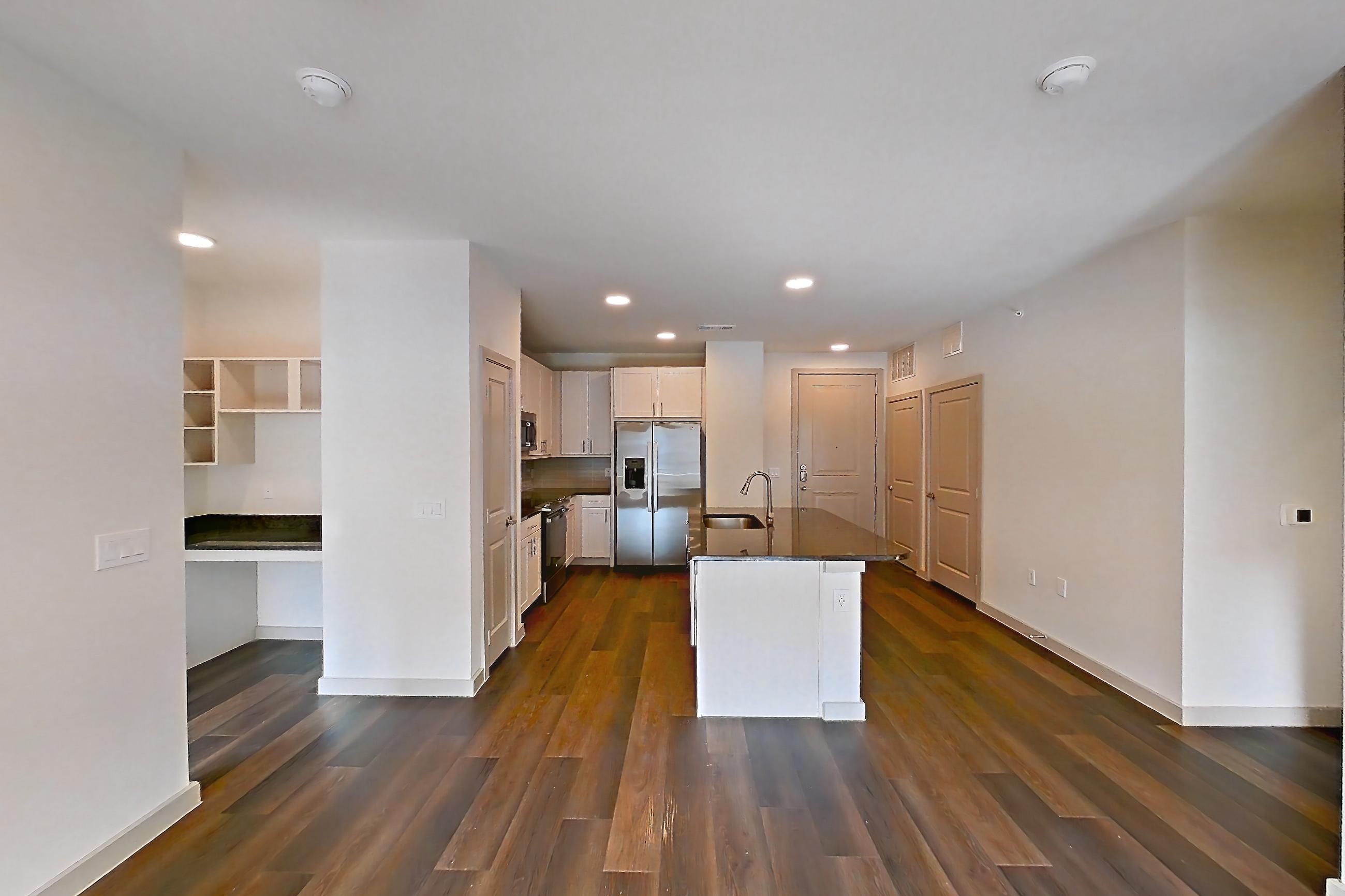 Living room with dark stone countertops, dark wood-finish flooring, electric range, kitchen island, refrigerator, and stainless steel appliances, Apartment 2230 at Merit Lewisville