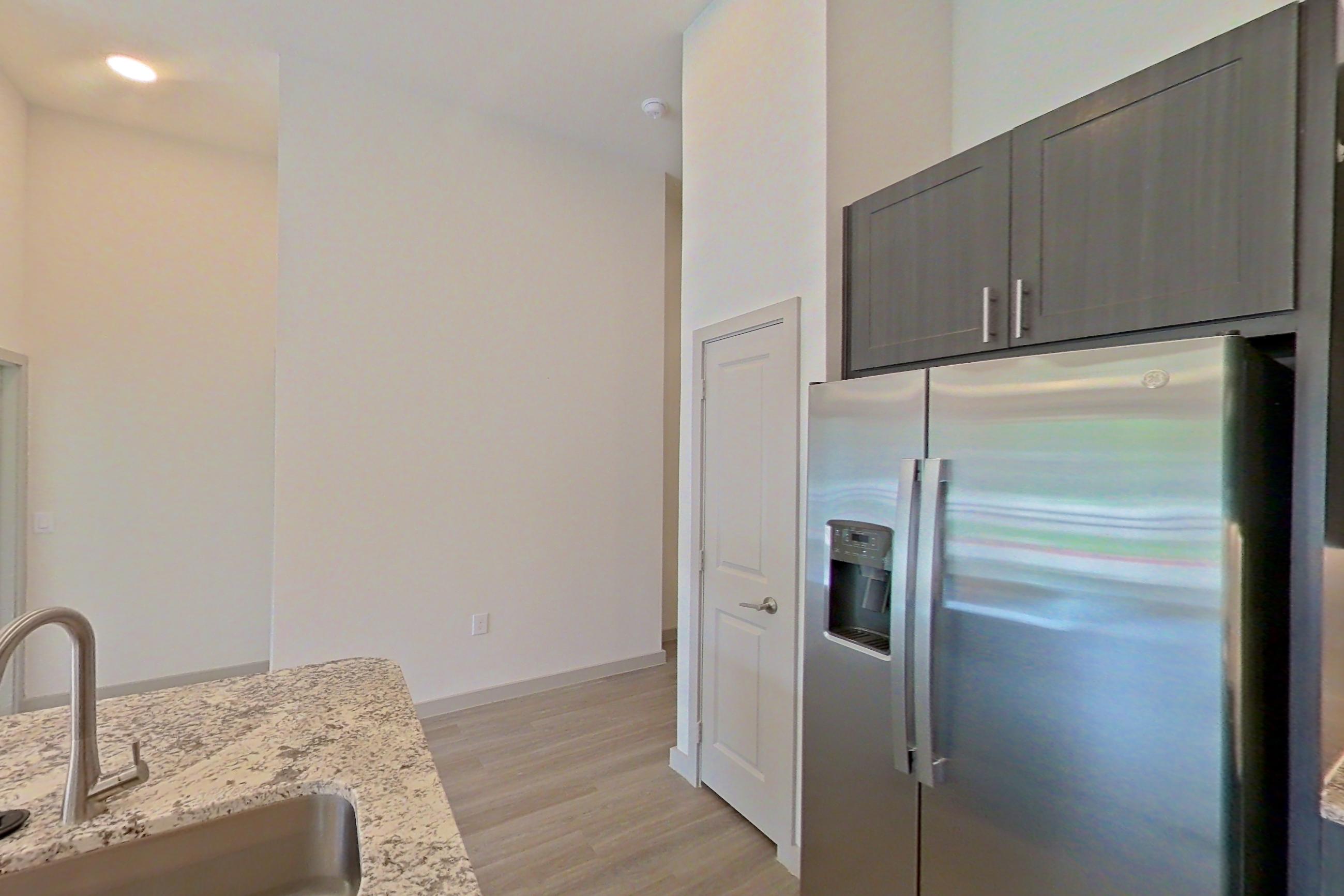 Kitchen with electric range, light countertops, light stone countertops, light wood-finish flooring, microwave, oven/range, refrigerator, stainless steel appliances, and water & ice dispenser, Apartment 2165 at Merit Lewisville