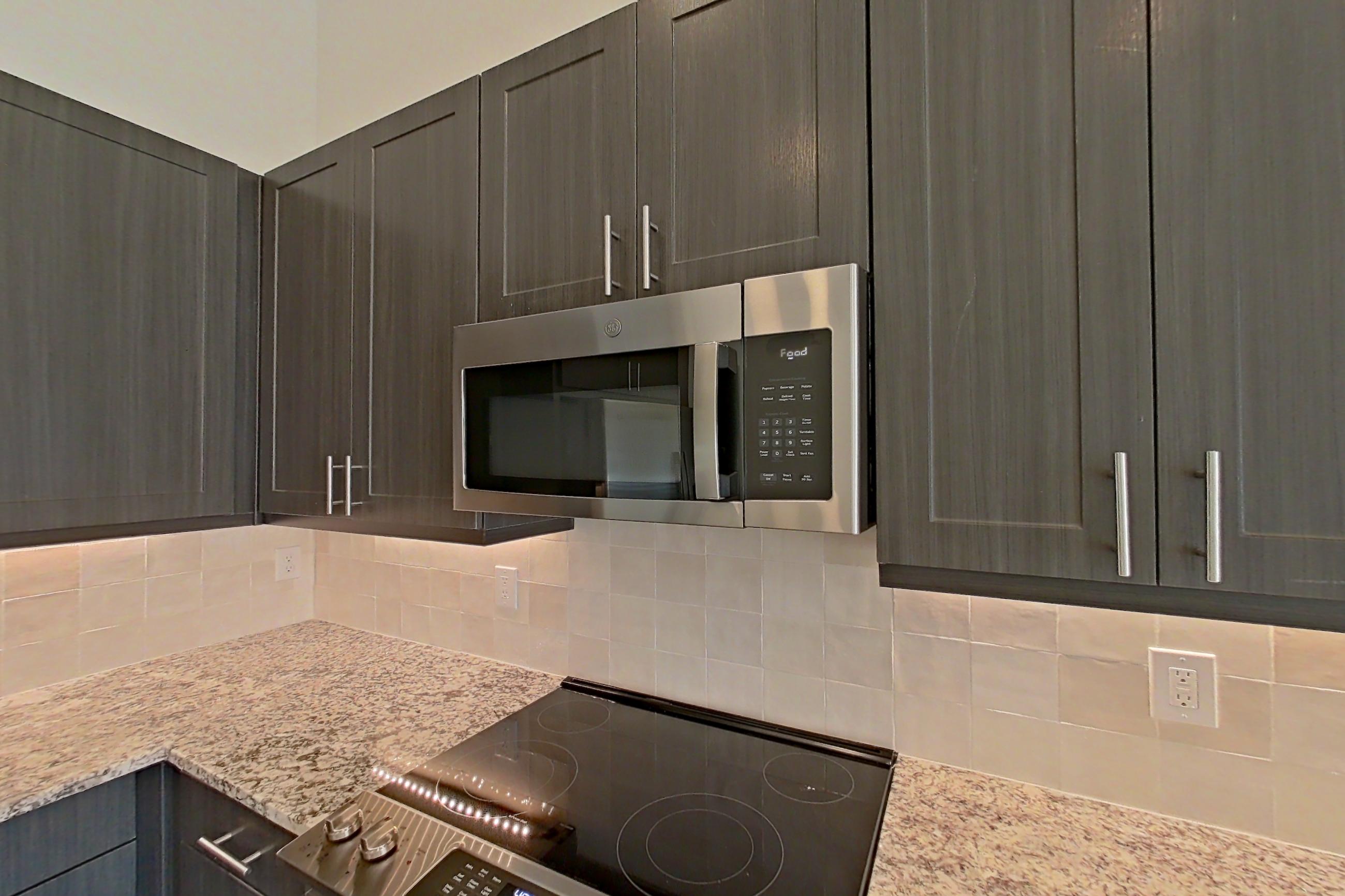 Kitchen with electric range, light countertops, light stone countertops, light wood-finish flooring, microwave, oven/range, refrigerator, stainless steel appliances, and water & ice dispenser, Apartment 2165 at Merit Lewisville