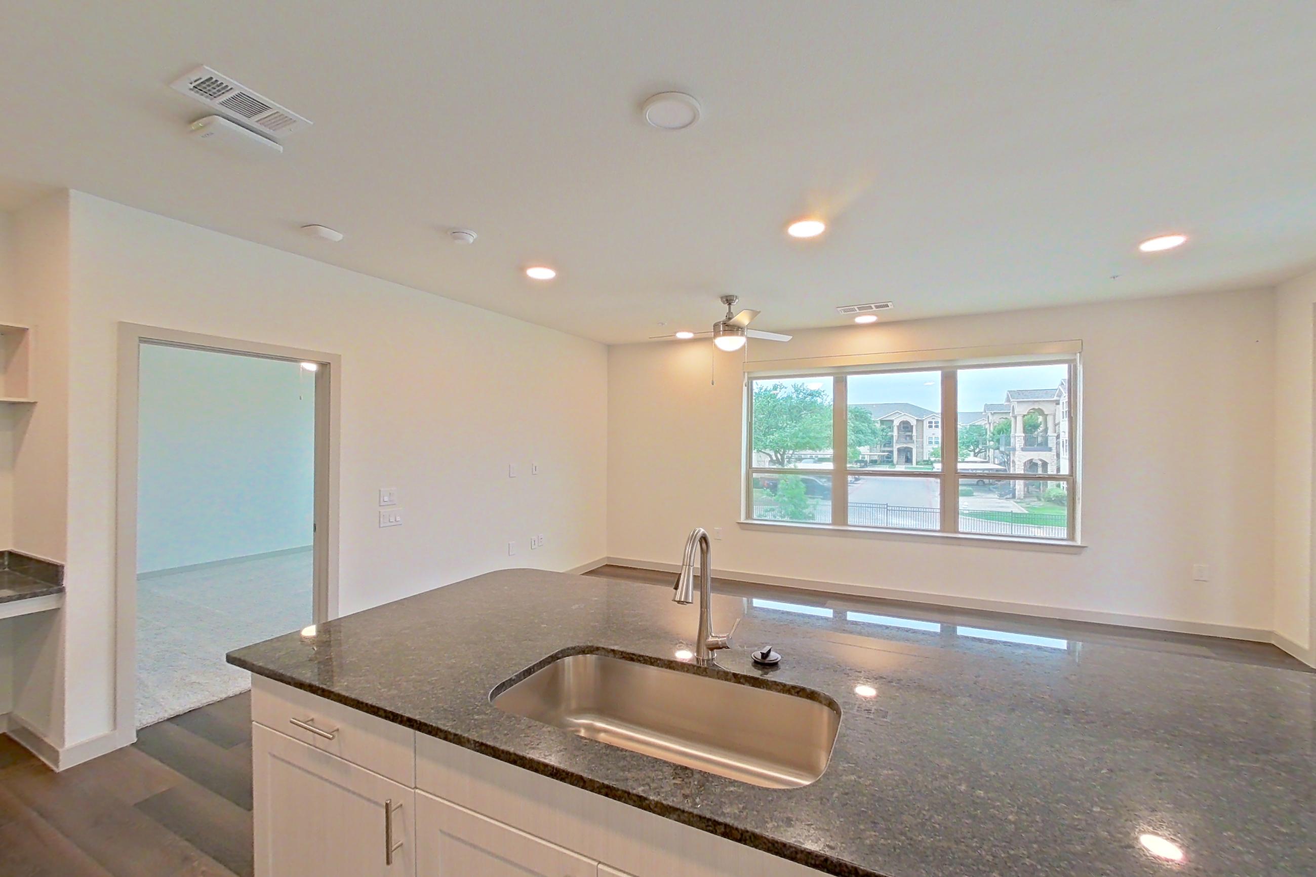 Kitchen with dark stone countertops, dark wood-finish flooring, dishwasher, electric range, oven/range, refrigerator, stainless steel appliances, and water & ice dispenser, Apartment 2225 at Merit Lewisville
