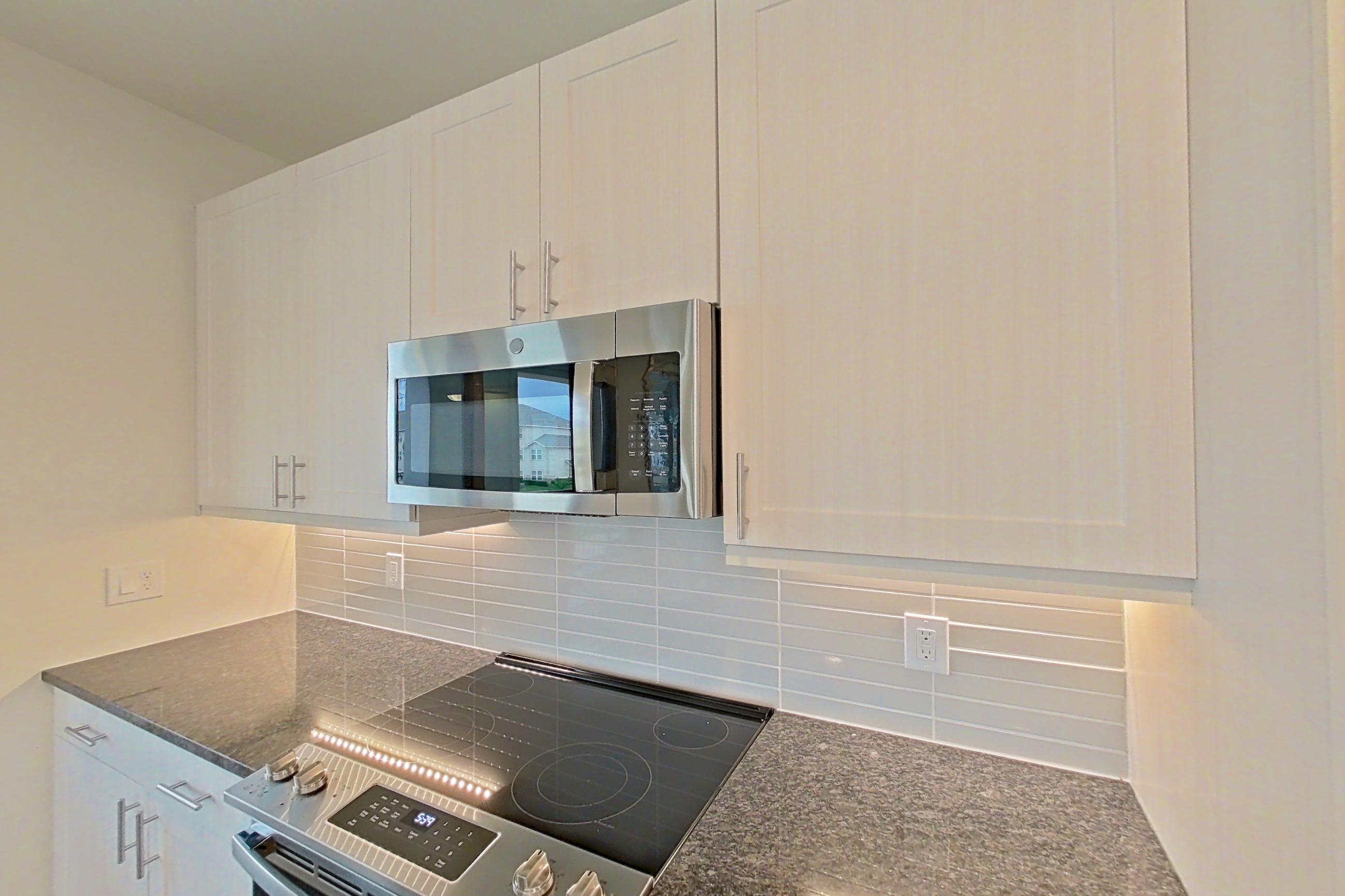 Kitchen with dark stone countertops, dark wood-finish flooring, dishwasher, electric range, oven/range, refrigerator, stainless steel appliances, and water & ice dispenser, Apartment 2225 at Merit Lewisville