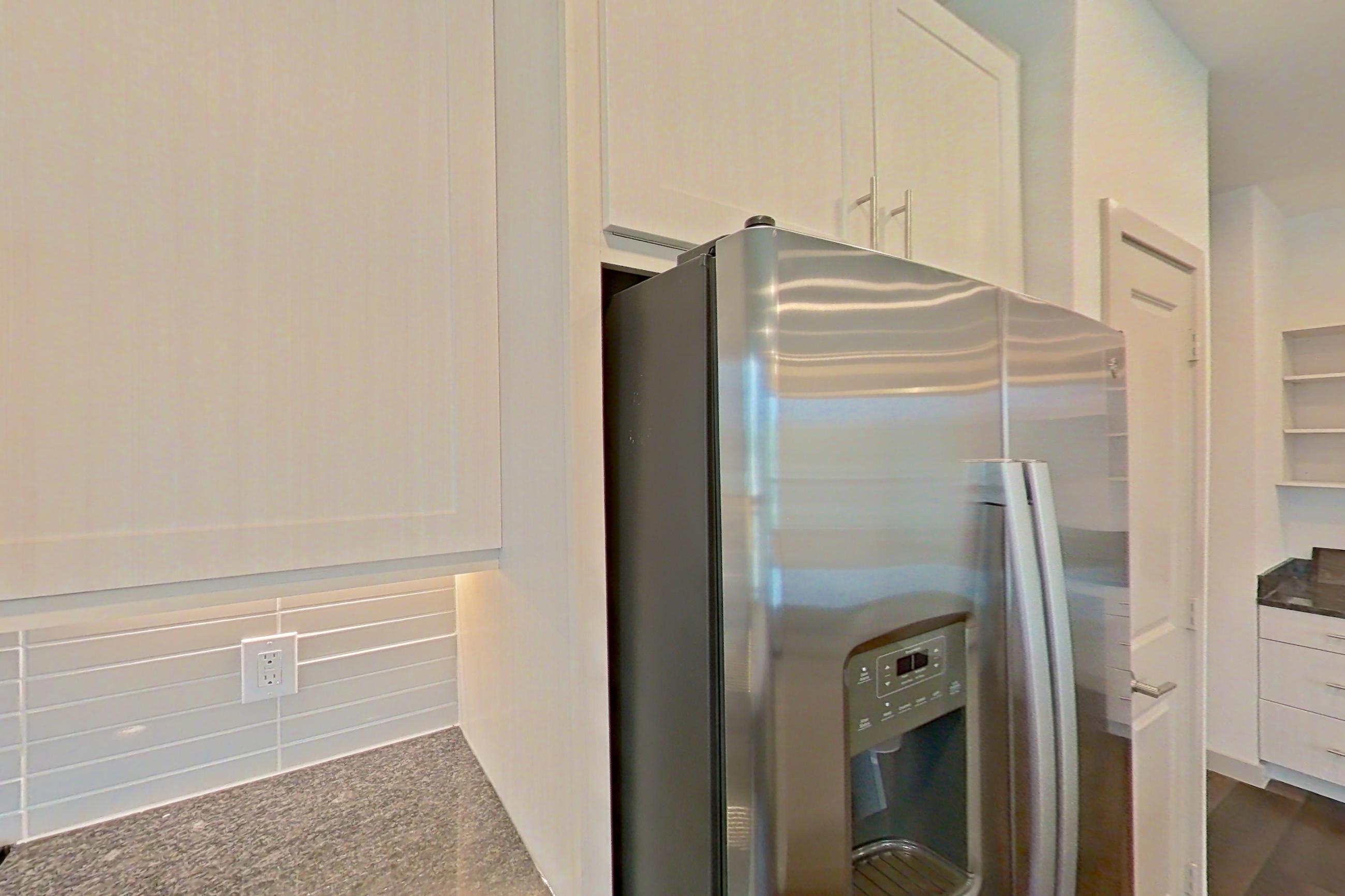 Kitchen with dark stone countertops, dark wood-finish flooring, dishwasher, electric range, oven/range, refrigerator, stainless steel appliances, and water & ice dispenser, Apartment 2225 at Merit Lewisville
