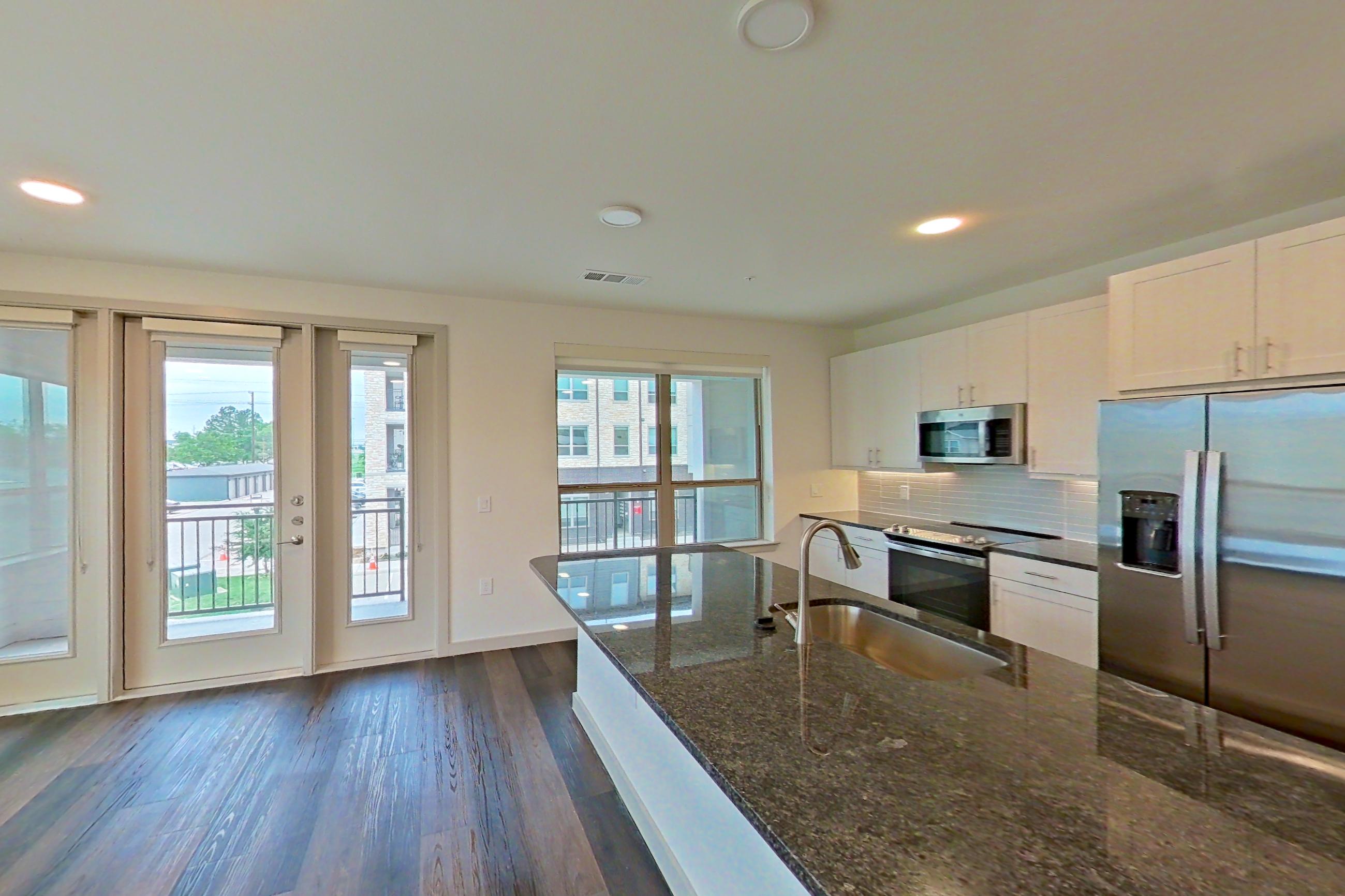 Living room with dark stone countertops, dark wood-finish flooring, electric range, fireplace, kitchen island, light countertops, oven/range, refrigerator, stainless steel appliances, and water & ice dispenser, Apartment 2225 at Merit Lewisville