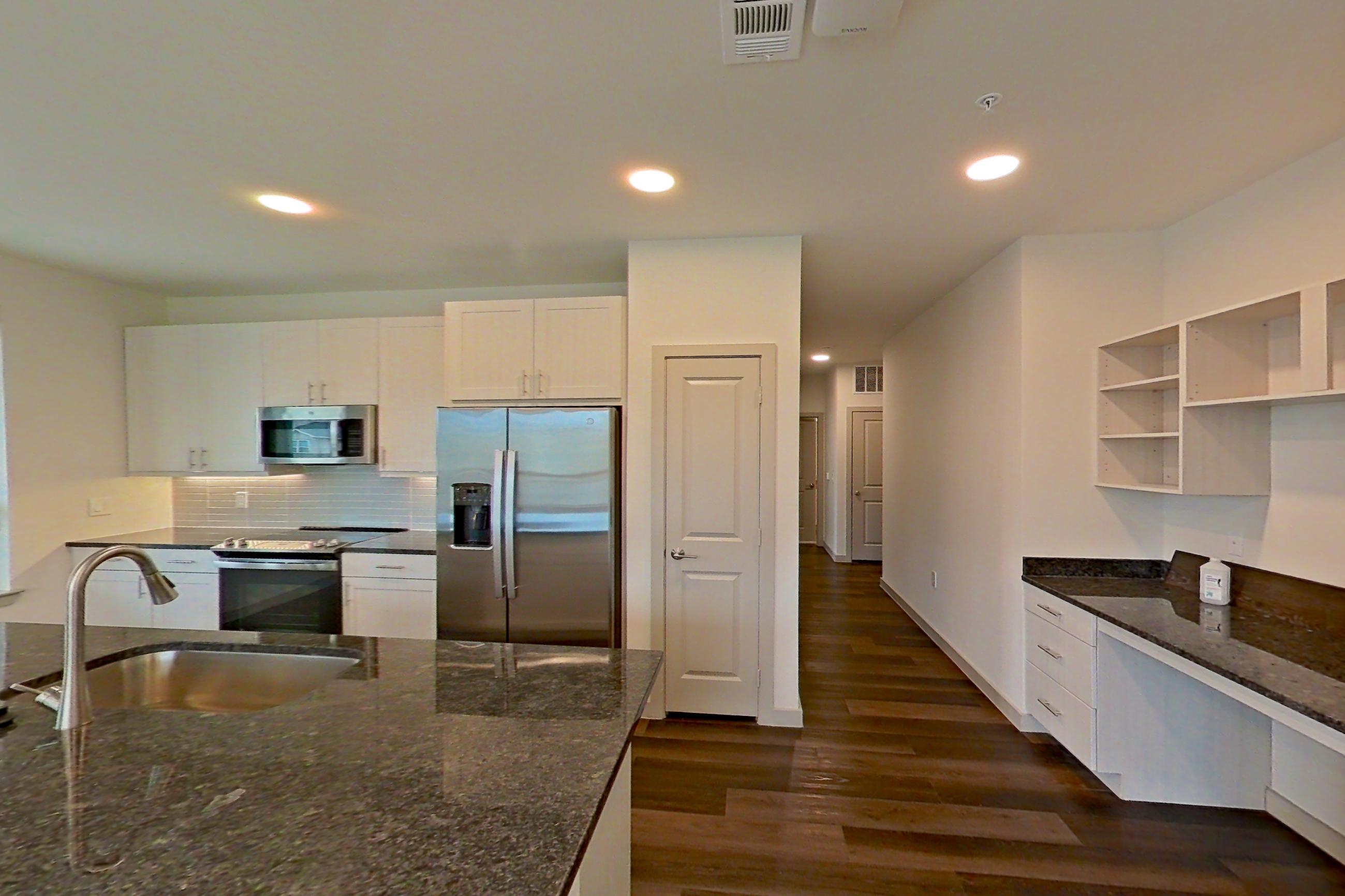 Living room with dark stone countertops, dark wood-finish flooring, electric range, fireplace, kitchen island, light countertops, oven/range, refrigerator, stainless steel appliances, and water & ice dispenser, Apartment 2225 at Merit Lewisville