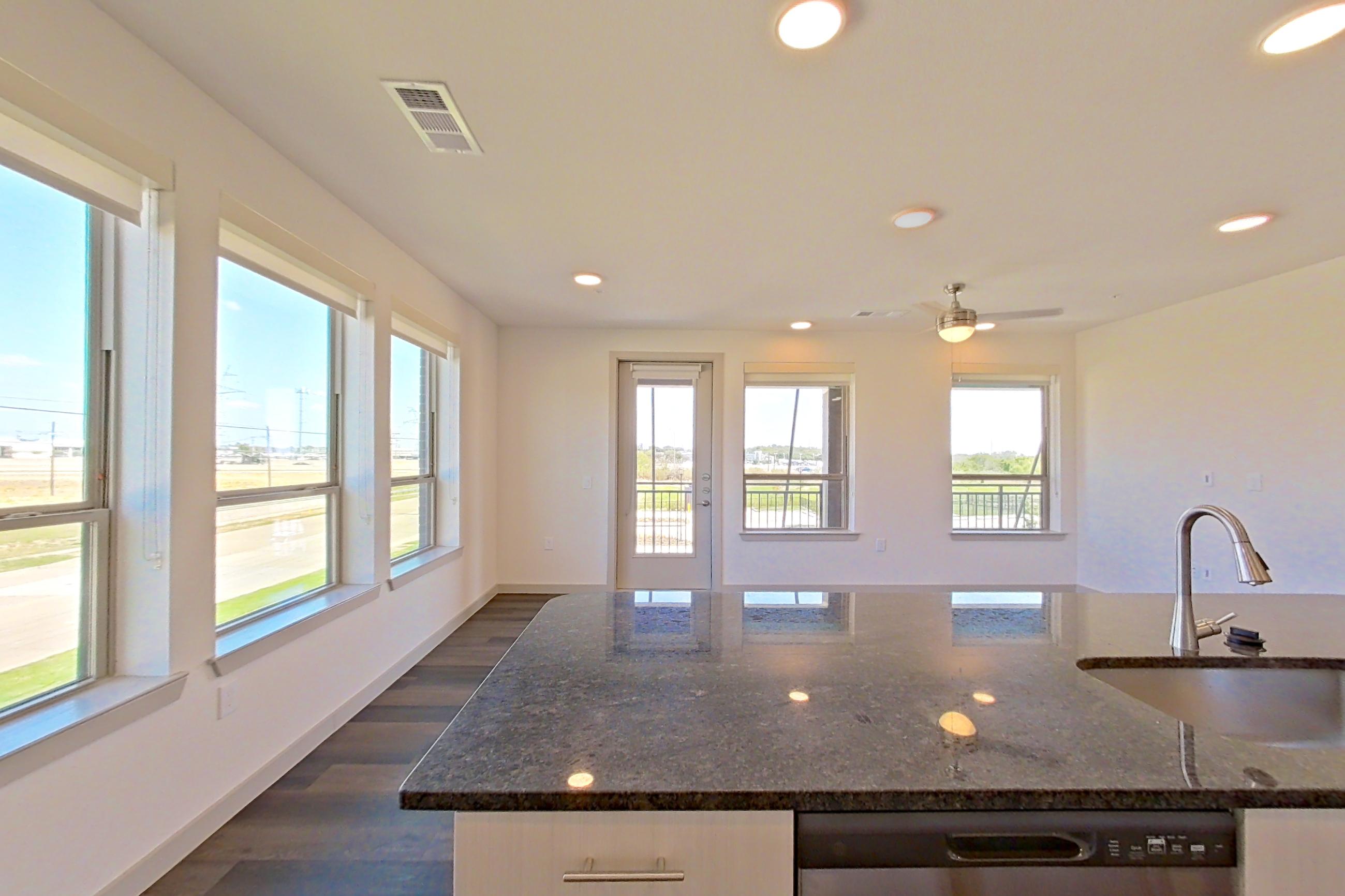 Kitchen with dark stone countertops, dark wood-finish flooring, dishwasher, electric range, microwave, oven/range, refrigerator, and stainless steel appliances, Apartment 1201 at Merit Lewisville