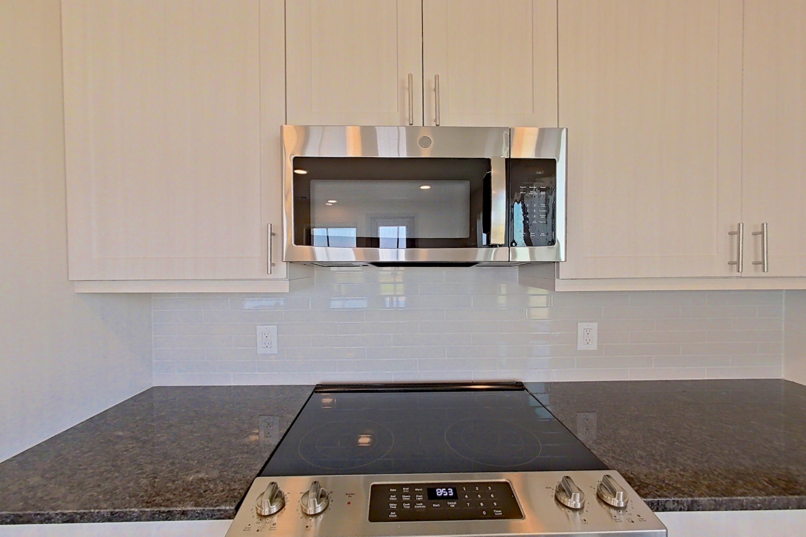 Kitchen with dark stone countertops, dark wood-finish flooring, dishwasher, electric range, microwave, oven/range, refrigerator, and stainless steel appliances, Apartment 1201 at Merit Lewisville