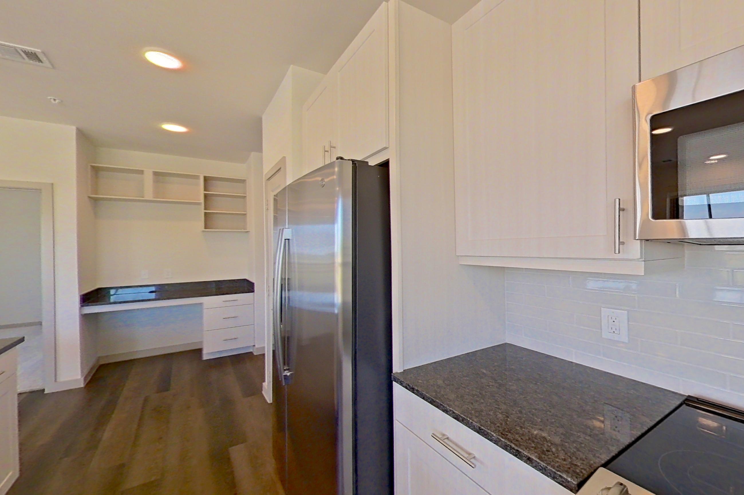 Kitchen with dark stone countertops, dark wood-finish flooring, dishwasher, electric range, microwave, oven/range, refrigerator, and stainless steel appliances, Apartment 1201 at Merit Lewisville