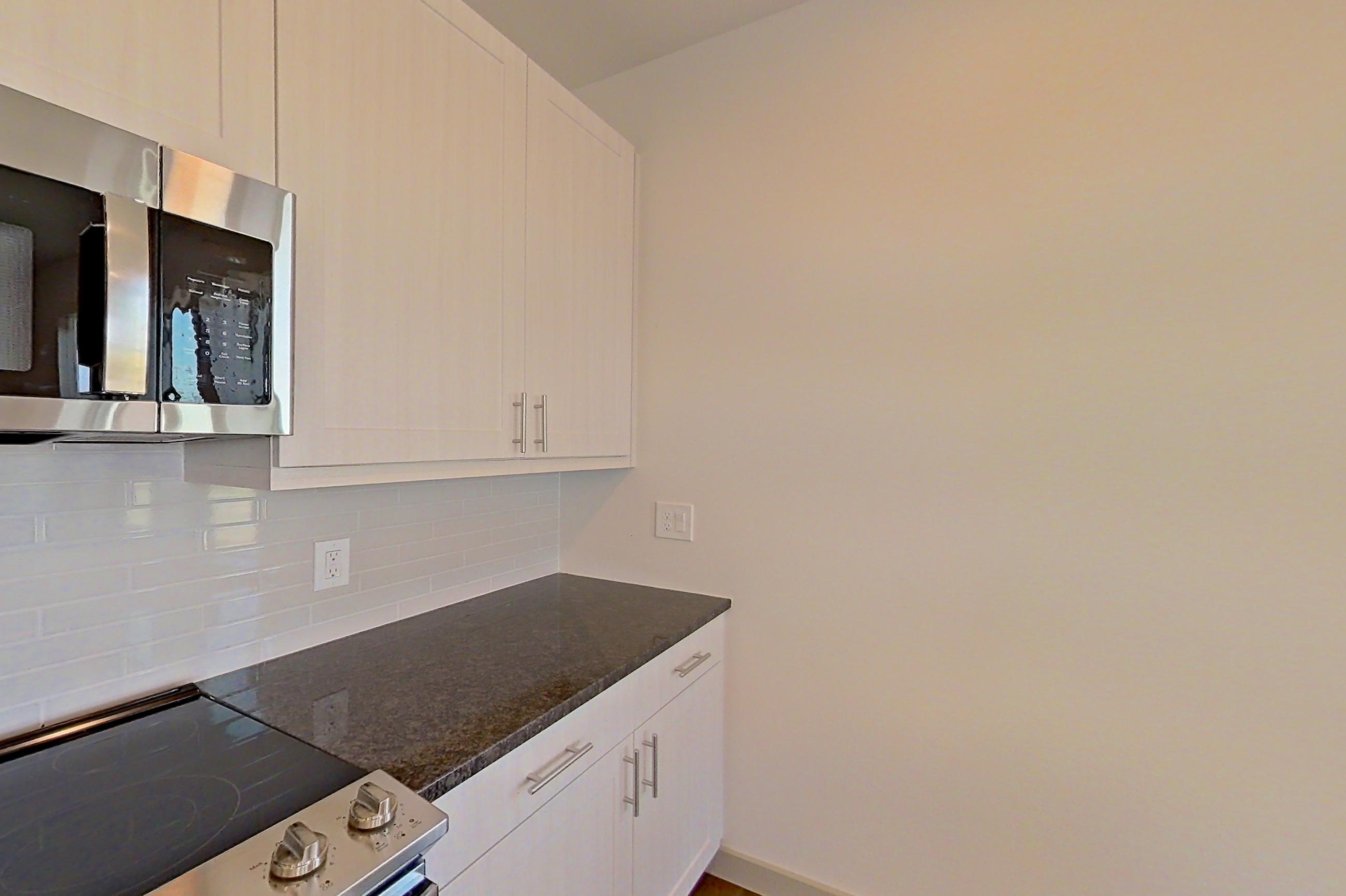 Kitchen with dark stone countertops, dark wood-finish flooring, dishwasher, electric range, microwave, oven/range, refrigerator, and stainless steel appliances, Apartment 1201 at Merit Lewisville