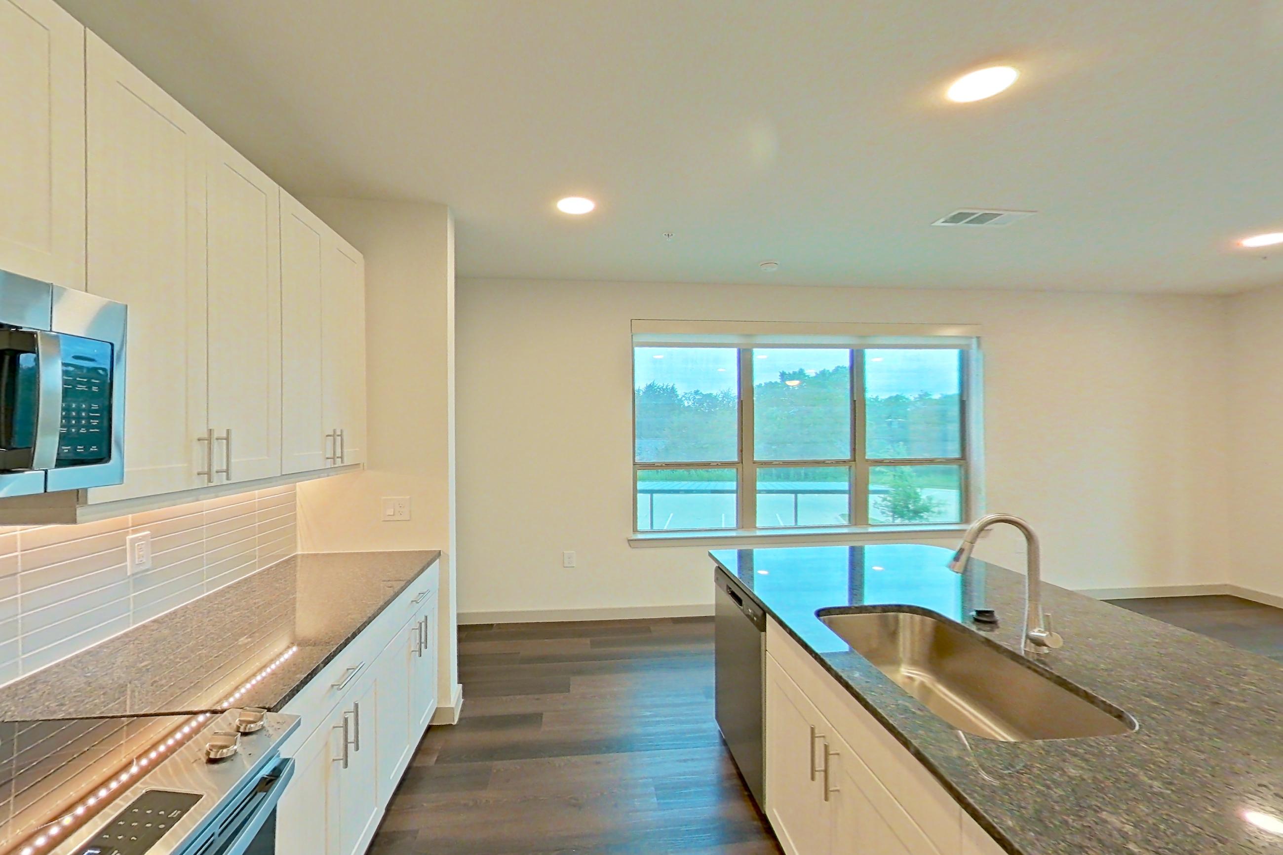 Kitchen with dark stone countertops, dark wood-finish flooring, dishwasher, electric range, microwave, oven/range, refrigerator, and stainless steel appliances, Apartment 2233 at Merit Lewisville