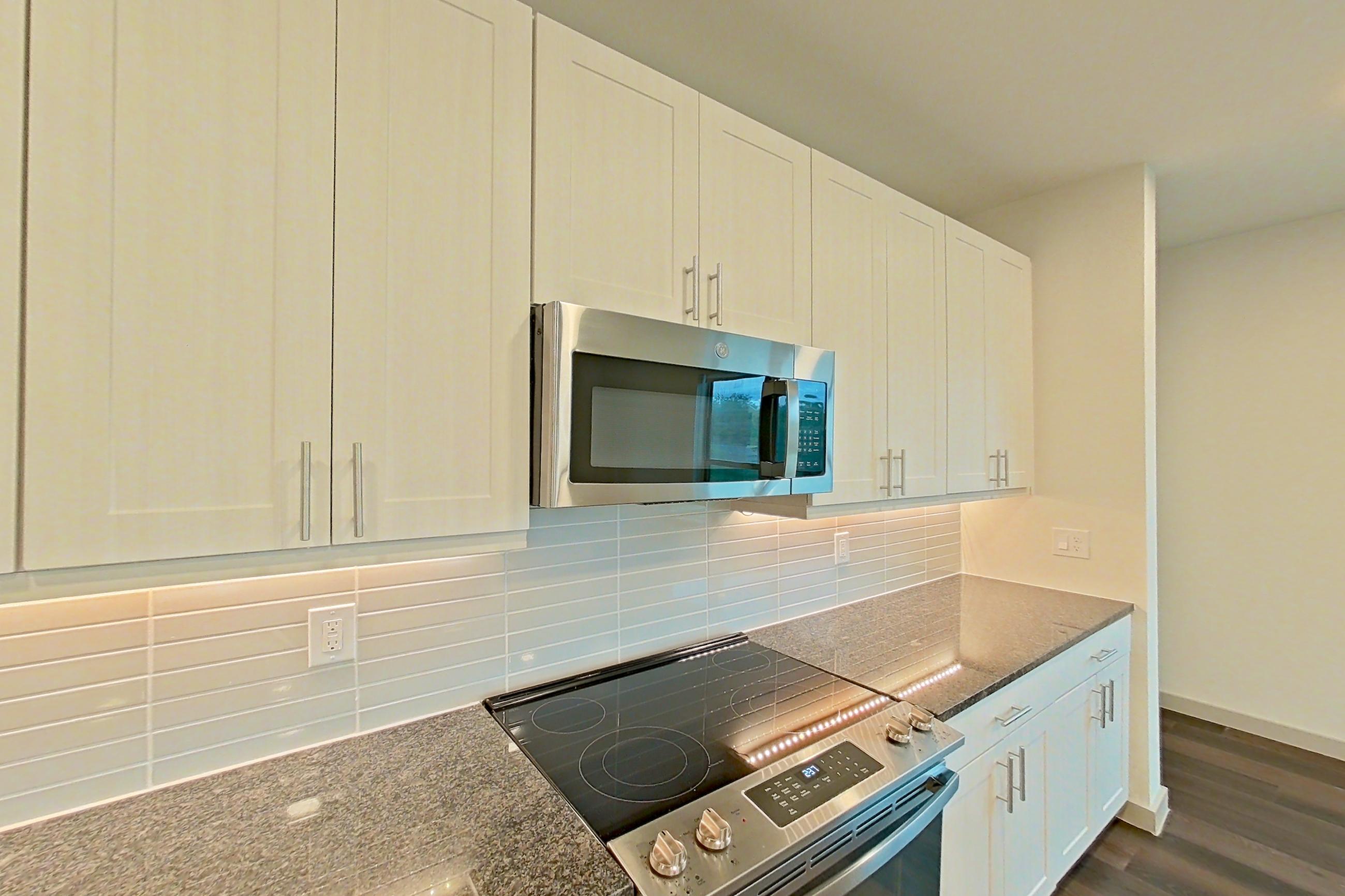 Kitchen with dark stone countertops, dark wood-finish flooring, dishwasher, electric range, microwave, oven/range, refrigerator, and stainless steel appliances, Apartment 2233 at Merit Lewisville