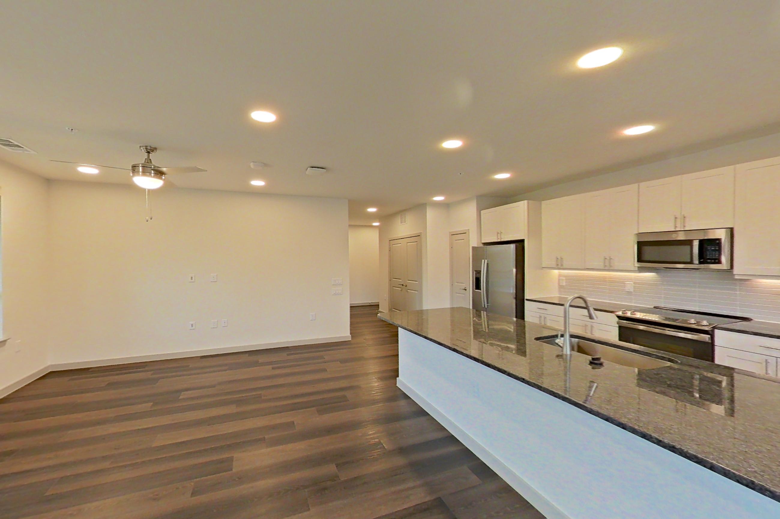 Living room with dark stone countertops, dark wood-finish flooring, electric range, kitchen island, oven/range, refrigerator, stainless steel appliances, and water & ice dispenser, Apartment 2233 at Merit Lewisville