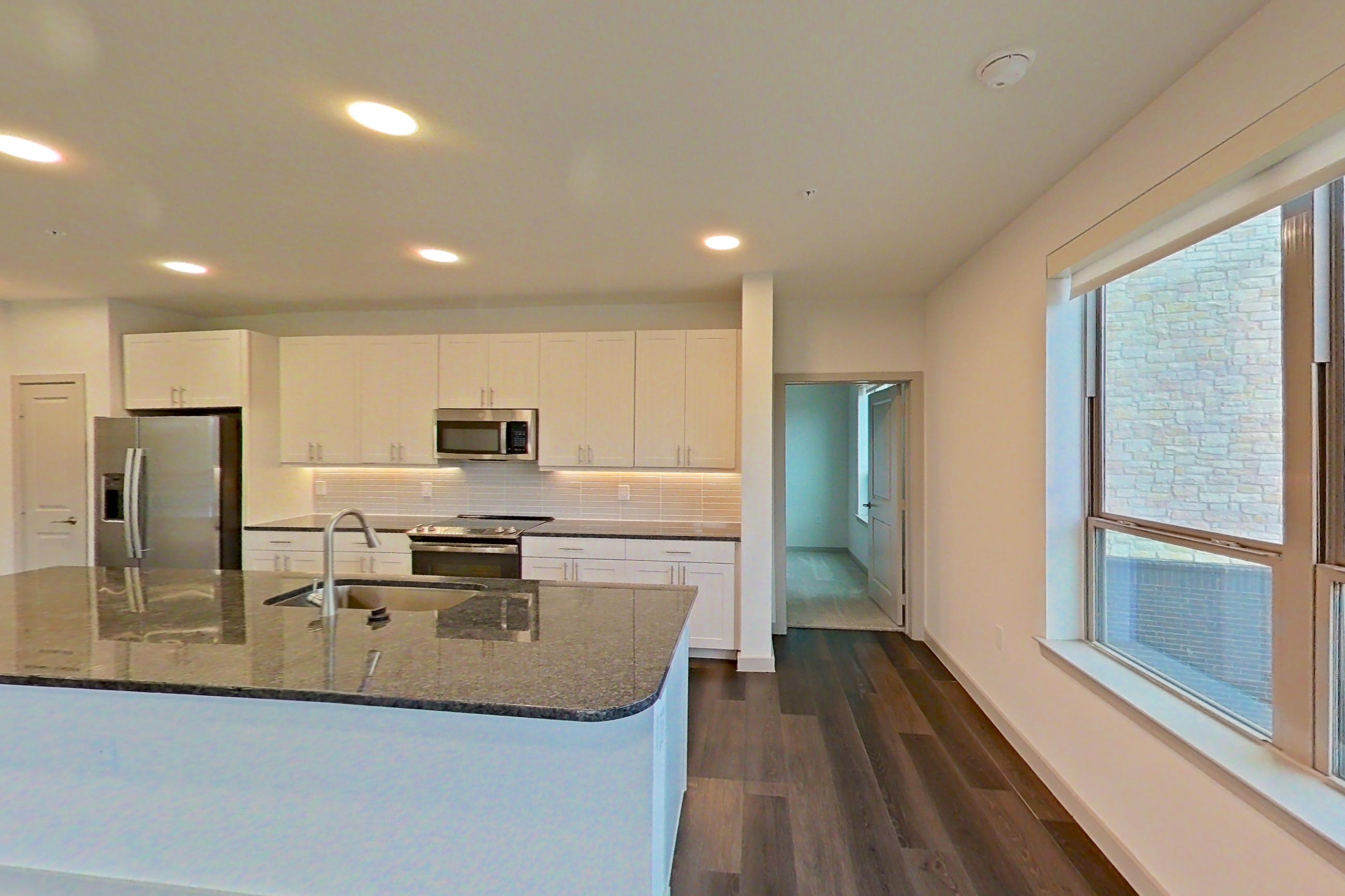 Living room with dark stone countertops, dark wood-finish flooring, electric range, kitchen island, oven/range, refrigerator, stainless steel appliances, and water & ice dispenser, Apartment 2233 at Merit Lewisville