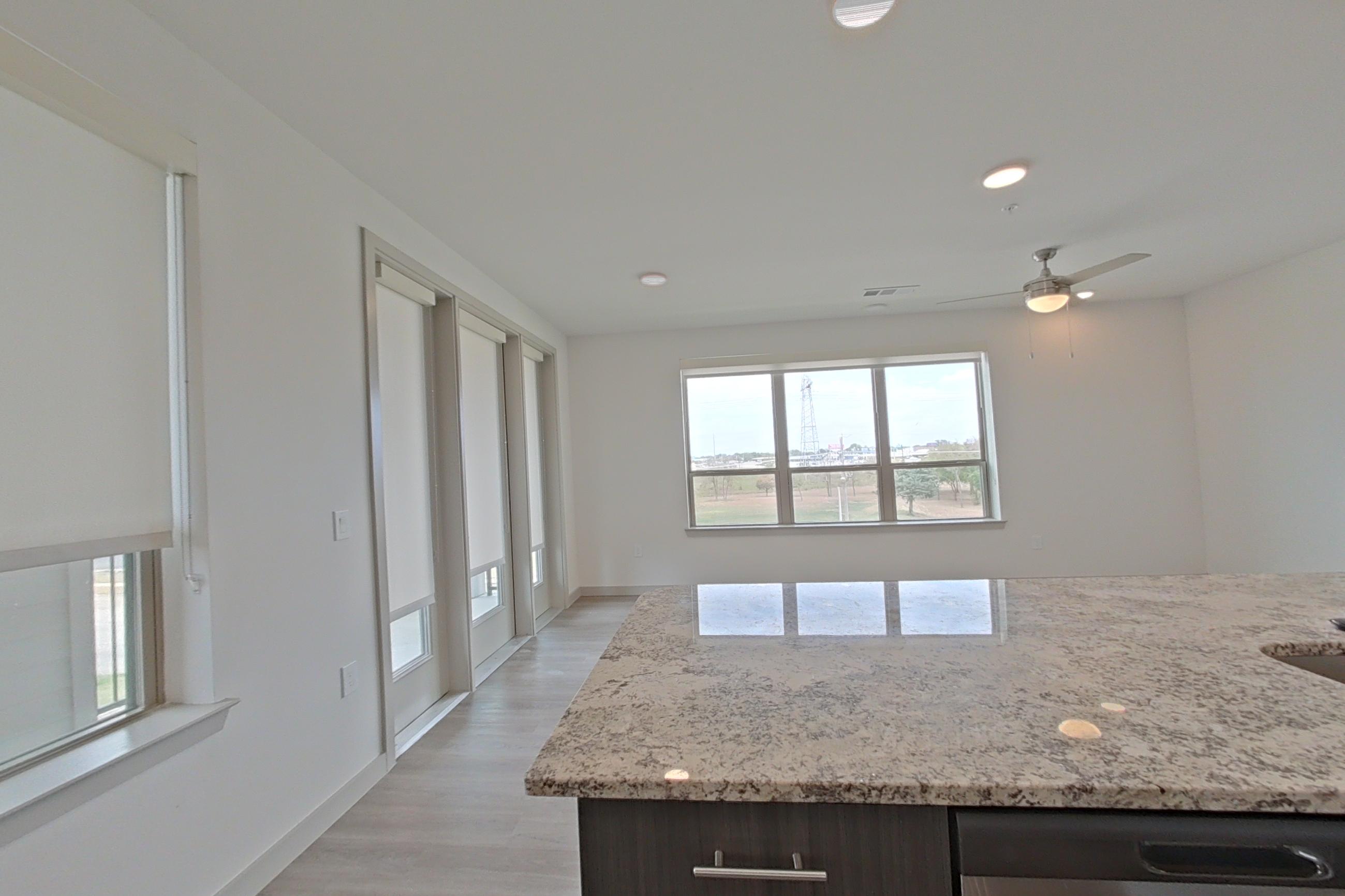 Kitchen with dishwasher, electric range, light stone countertops, light wood-finish flooring, microwave, oven/range, refrigerator, and stainless steel appliances, Apartment 1305 at Merit Lewisville