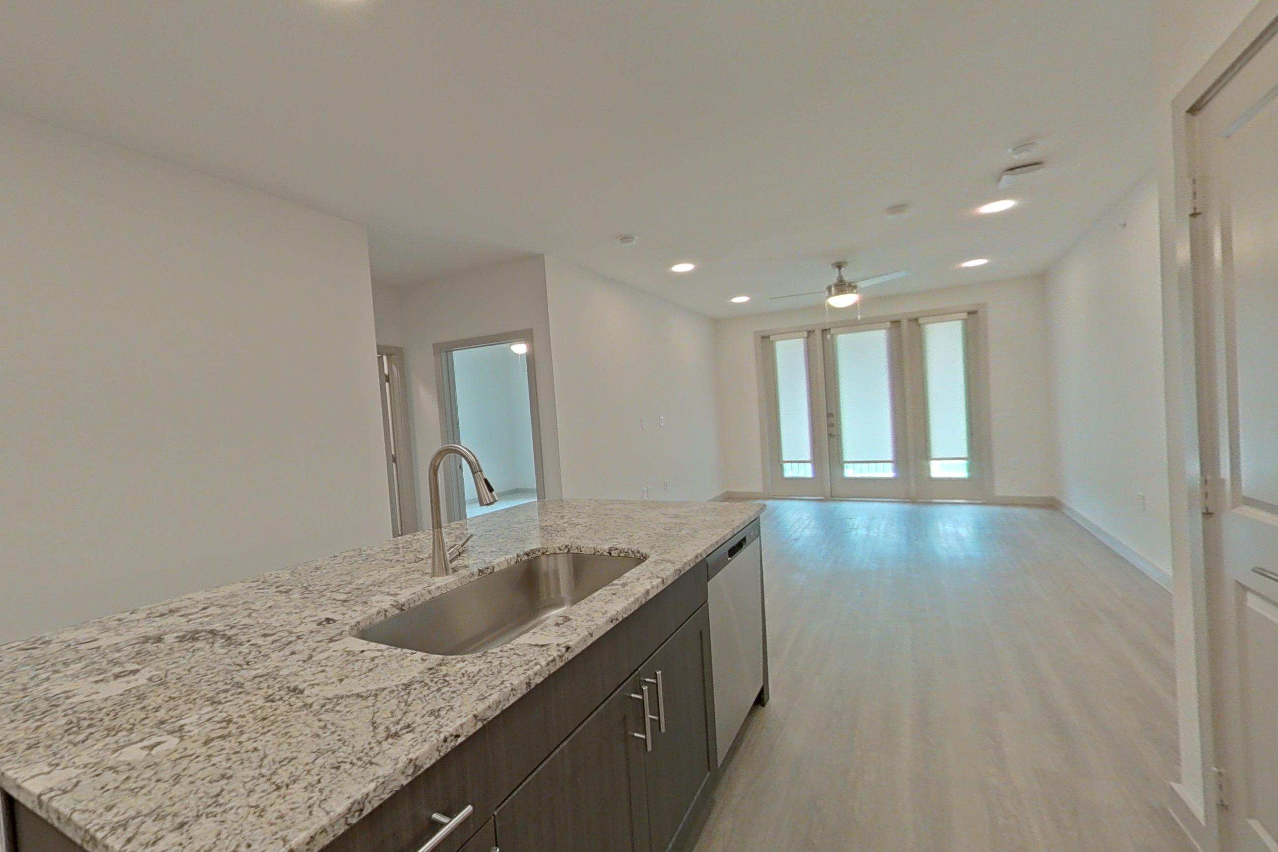 Kitchen with electric range, light stone countertops, light wood-finish flooring, microwave, oven/range, refrigerator, stainless steel appliances, and water & ice dispenser, Apartment 1310 at Merit Lewisville