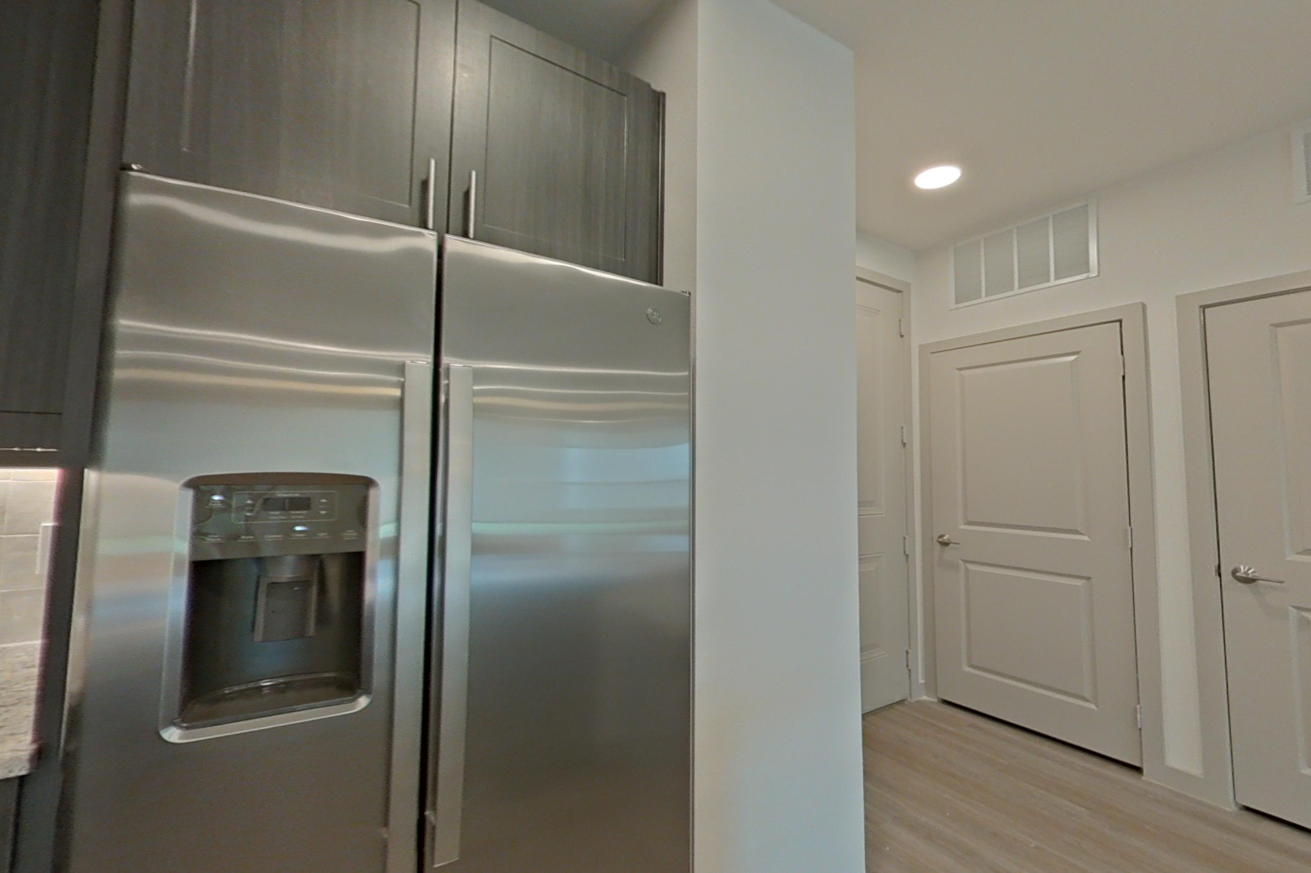 Kitchen with electric range, light stone countertops, light wood-finish flooring, microwave, oven/range, refrigerator, stainless steel appliances, and water & ice dispenser, Apartment 1310 at Merit Lewisville
