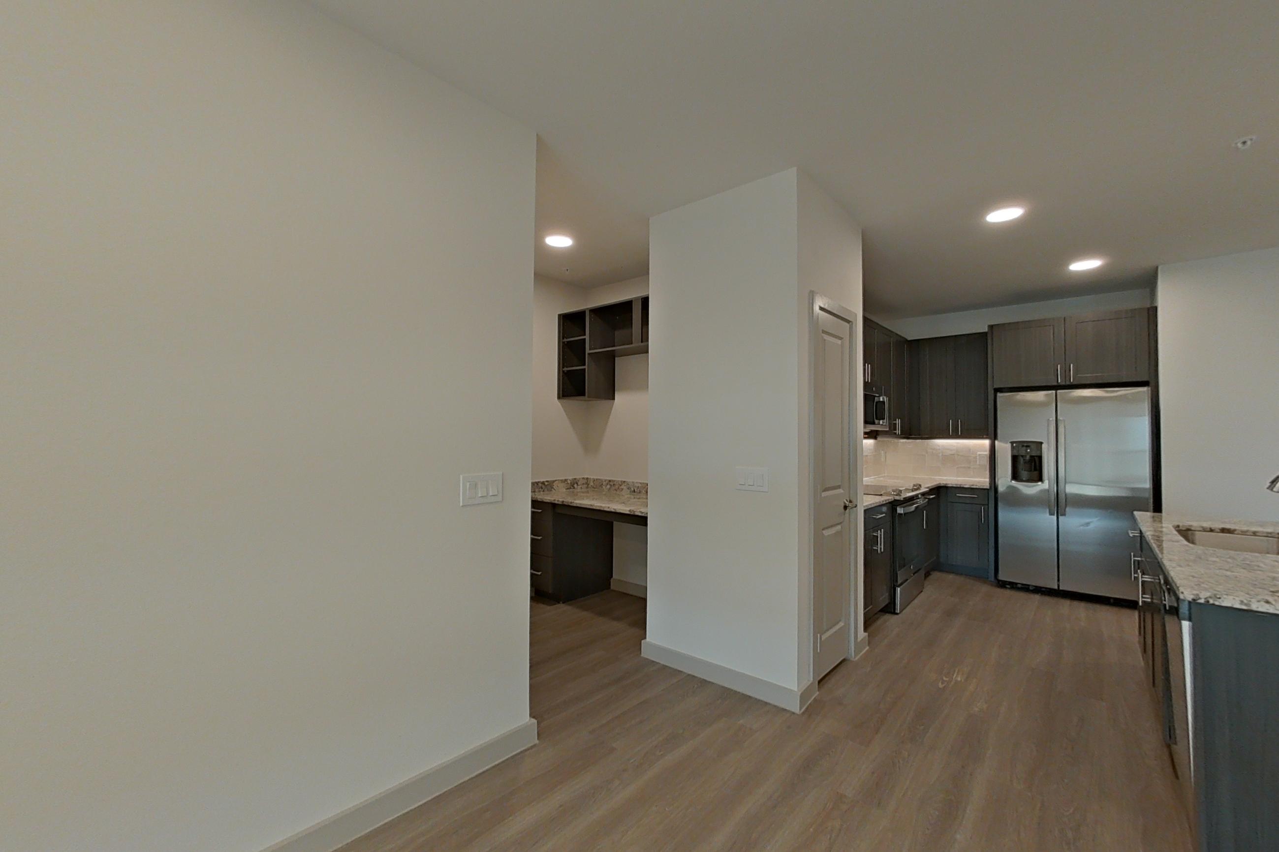 Living room with light wood-finish flooring, refrigerator, and stainless steel appliances, Apartment 1310 at Merit Lewisville