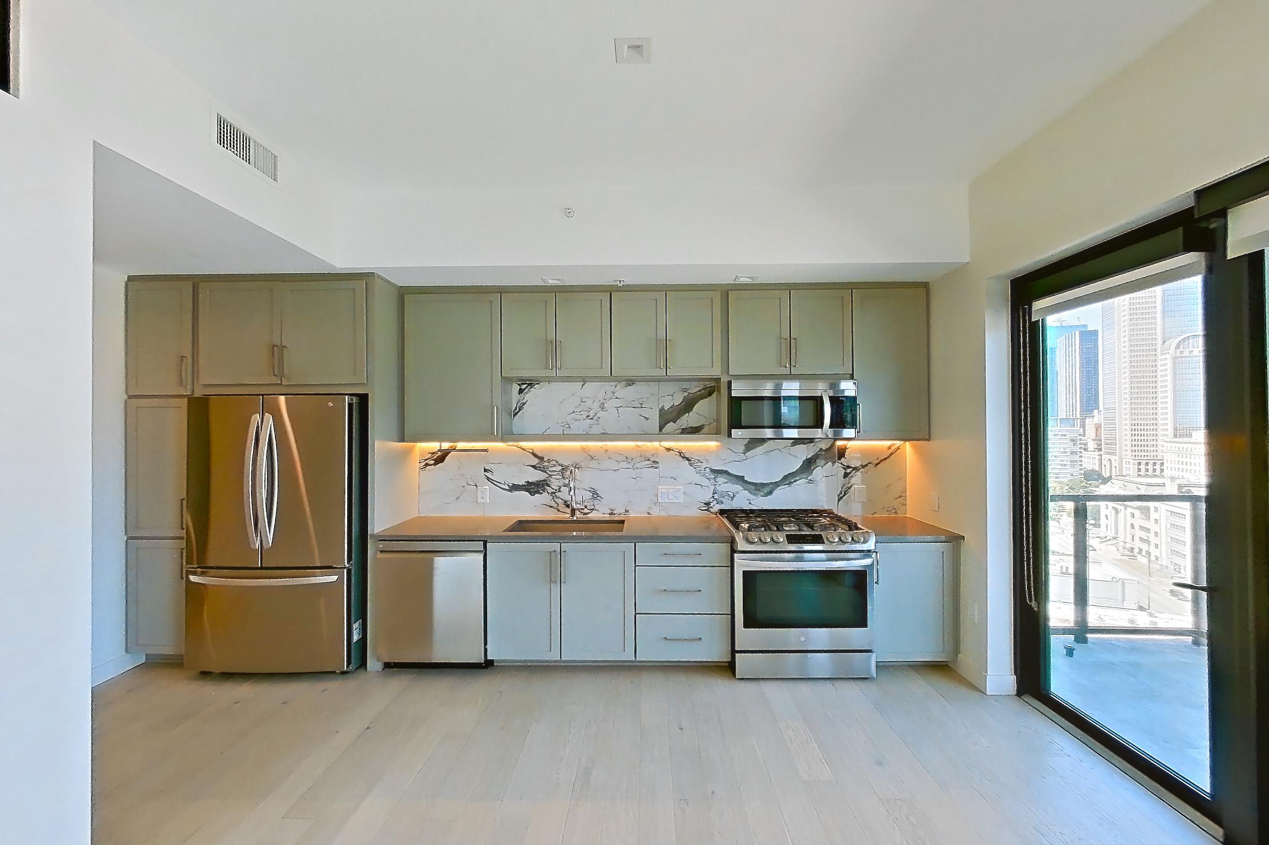 Living space with dark countertops, gas range, light wood-finish flooring, oven/range, refrigerator, skyline view, and stainless steel appliances, Apartment 1028 at East Quarter Residences