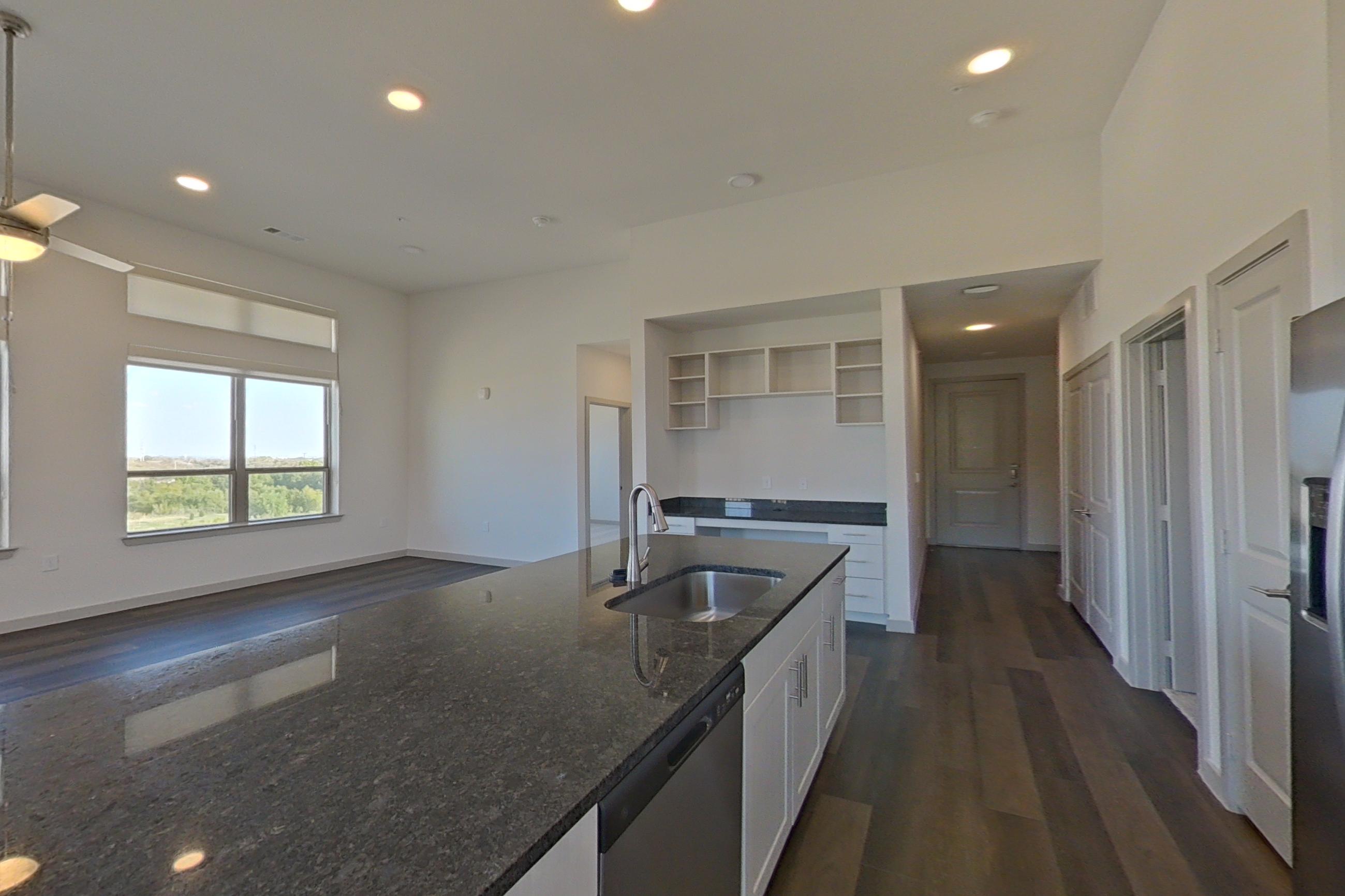 Kitchen with dark stone countertops, dark wood-finish flooring, dishwasher, electric range, microwave, oven/range, refrigerator, and stainless steel appliances, Apartment 1418 at Merit Lewisville