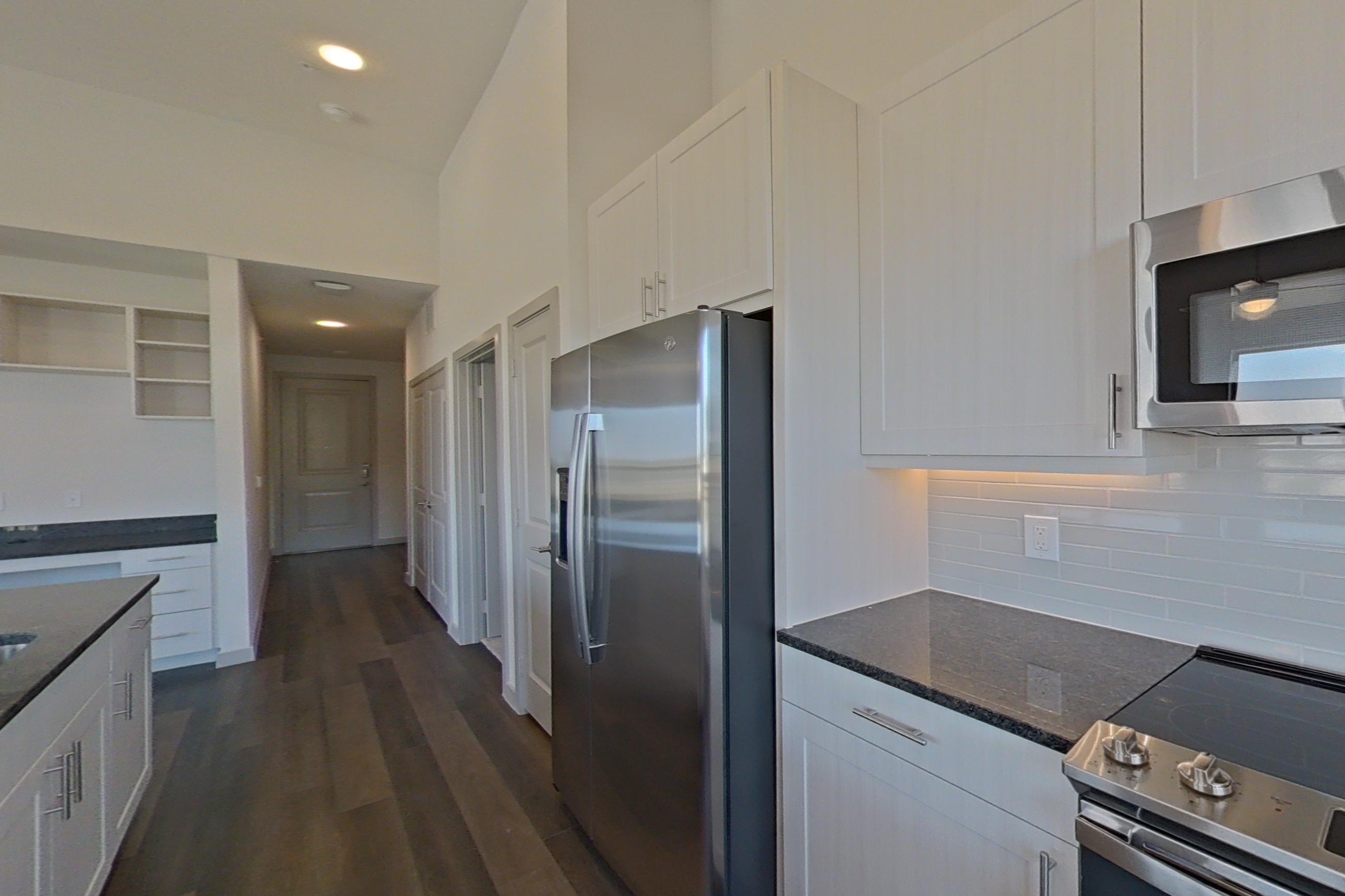 Kitchen with dark stone countertops, dark wood-finish flooring, dishwasher, electric range, microwave, oven/range, refrigerator, and stainless steel appliances, Apartment 1418 at Merit Lewisville