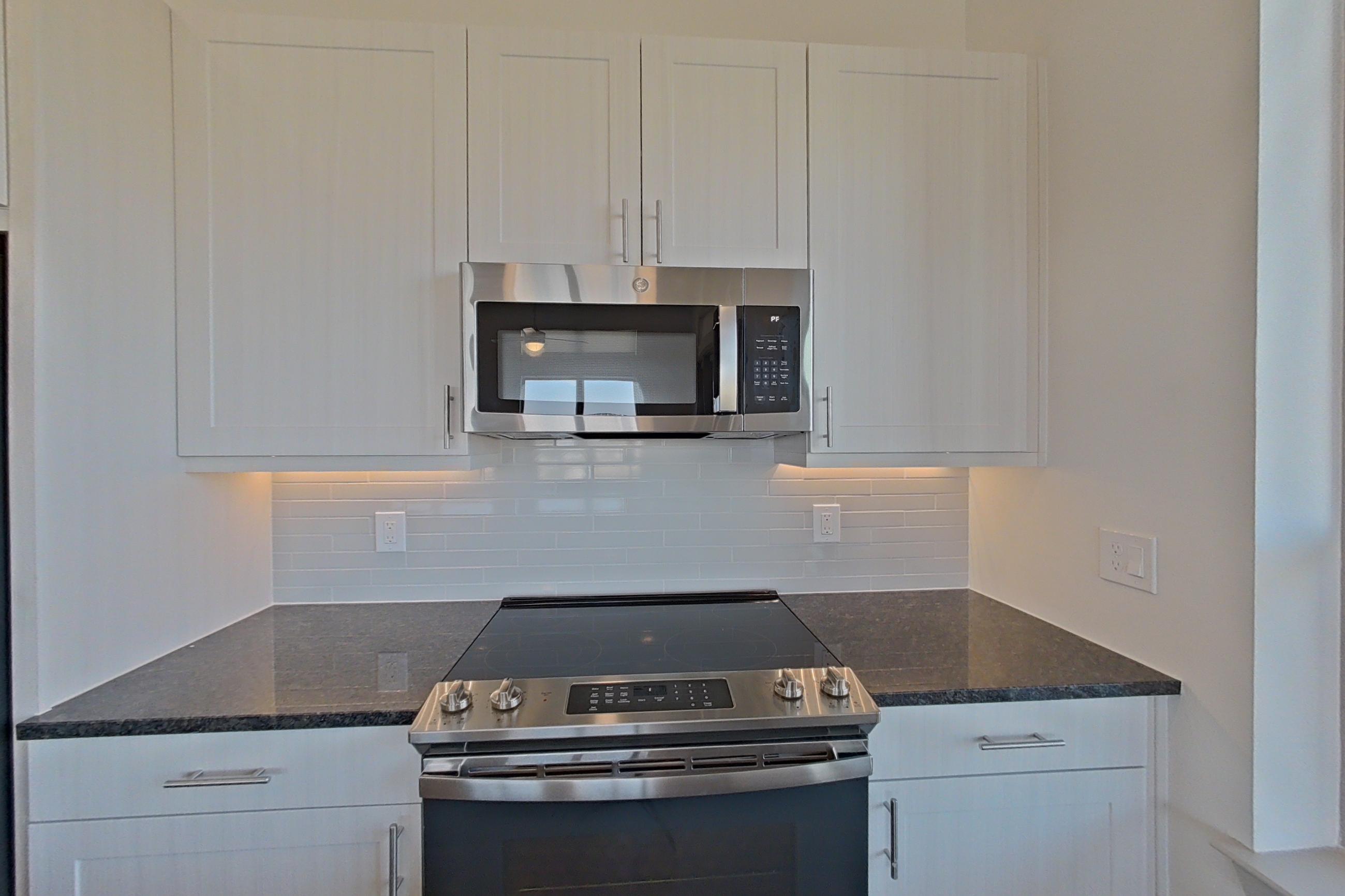 Kitchen with dark stone countertops, dark wood-finish flooring, dishwasher, electric range, microwave, oven/range, refrigerator, and stainless steel appliances, Apartment 1418 at Merit Lewisville