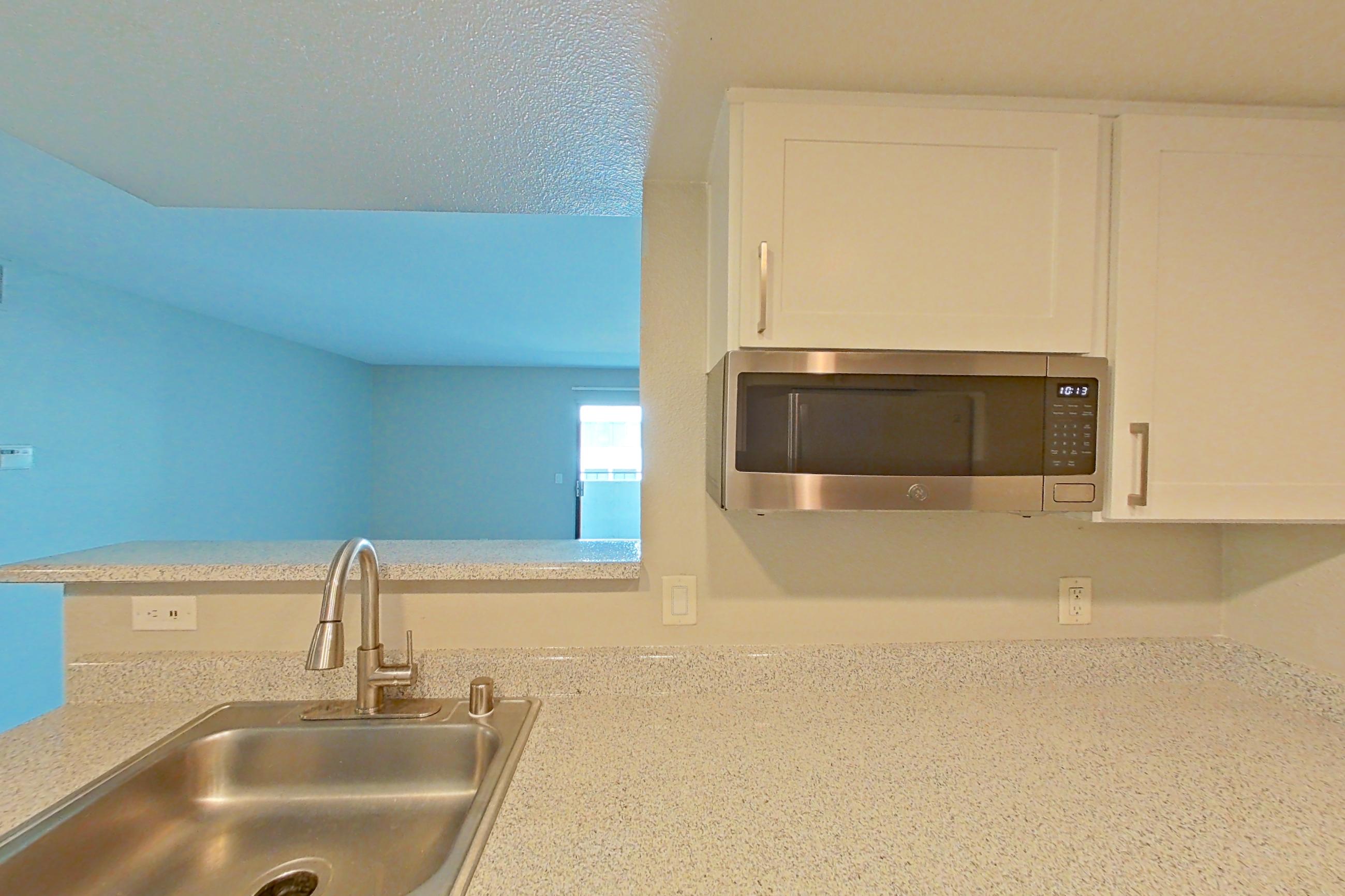 Kitchen with dishwasher, light stone countertops, light wood-finish flooring, microwave, refrigerator, and stainless steel appliances, Apartment 11 at Avana Rancho Cucamonga