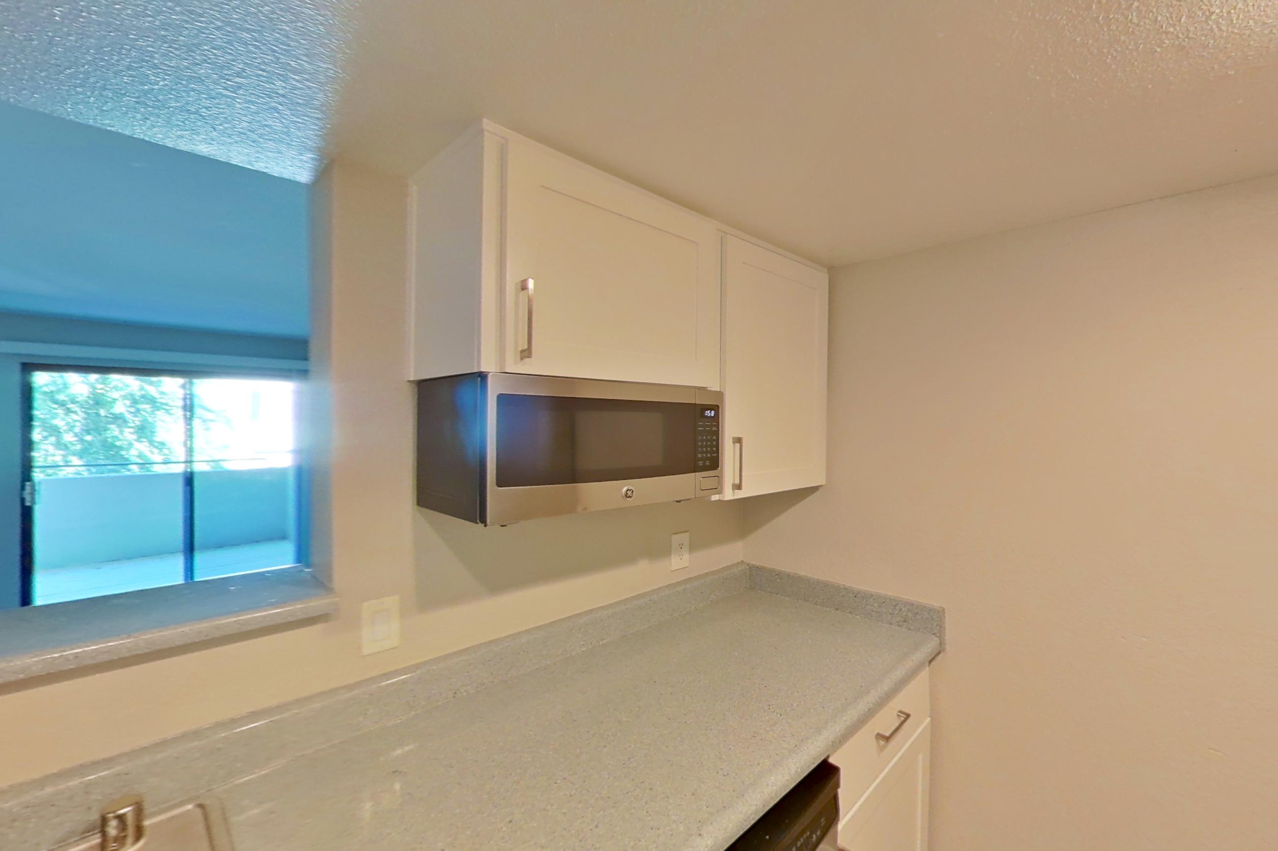 Kitchen with dishwasher, electric range, light countertops, light stone countertops, light wood-finish flooring, microwave, oven/range, refrigerator, stainless steel appliances, and white appliances, Apartment 23 at Avana Rancho Cucamonga