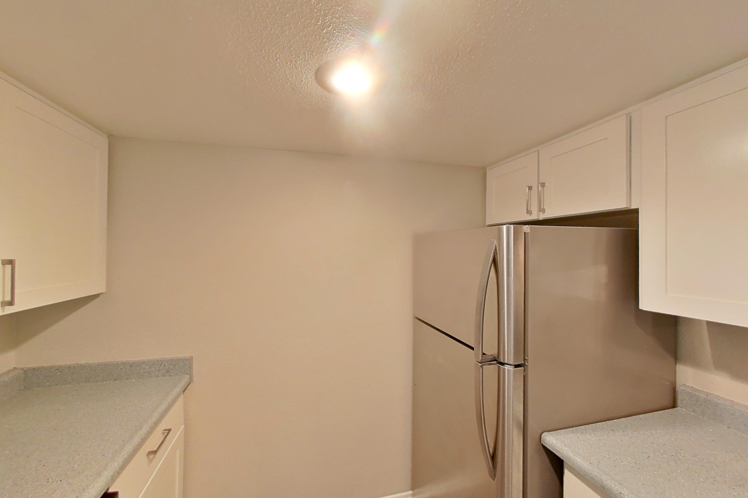 Kitchen with dishwasher, electric range, light countertops, light stone countertops, light wood-finish flooring, microwave, oven/range, refrigerator, stainless steel appliances, and white appliances, Apartment 23 at Avana Rancho Cucamonga