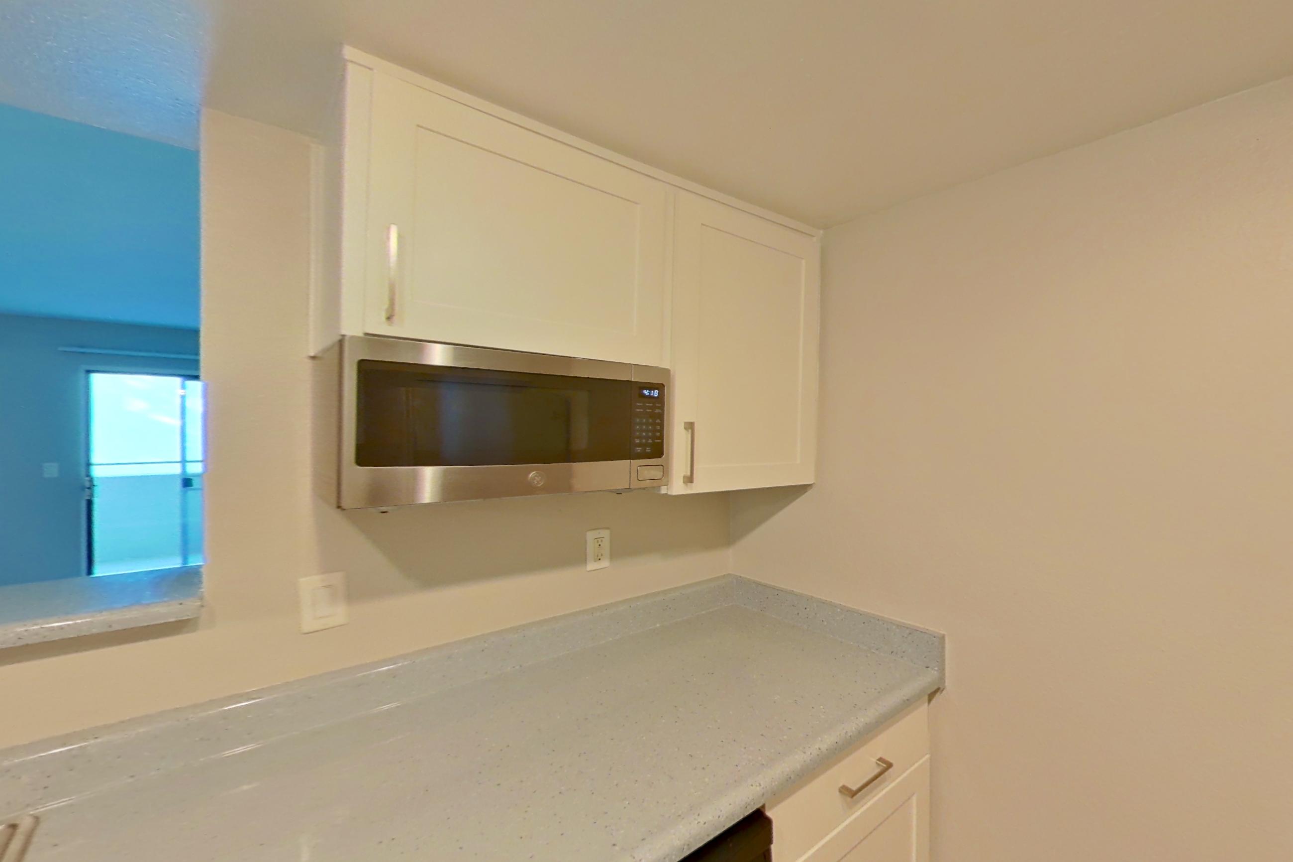 Kitchen with dishwasher, electric range, light countertops, light stone countertops, light wood-finish flooring, microwave, oven/range, range hood, refrigerator, stainless steel appliances, and white appliances, Apartment 06 at Avana Rancho Cucamonga