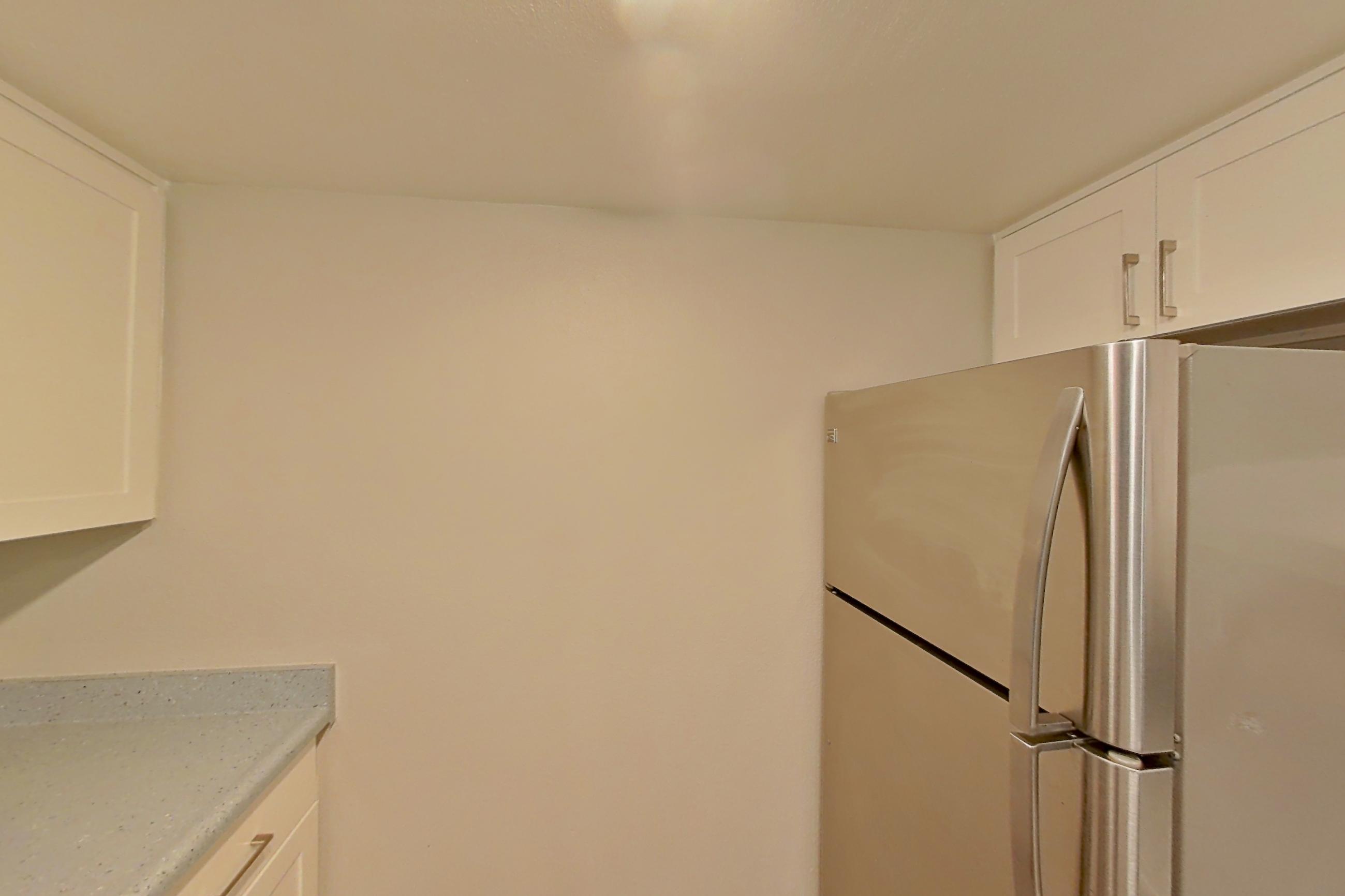 Kitchen with dishwasher, electric range, light countertops, light stone countertops, light wood-finish flooring, microwave, oven/range, range hood, refrigerator, stainless steel appliances, and white appliances, Apartment 06 at Avana Rancho Cucamonga