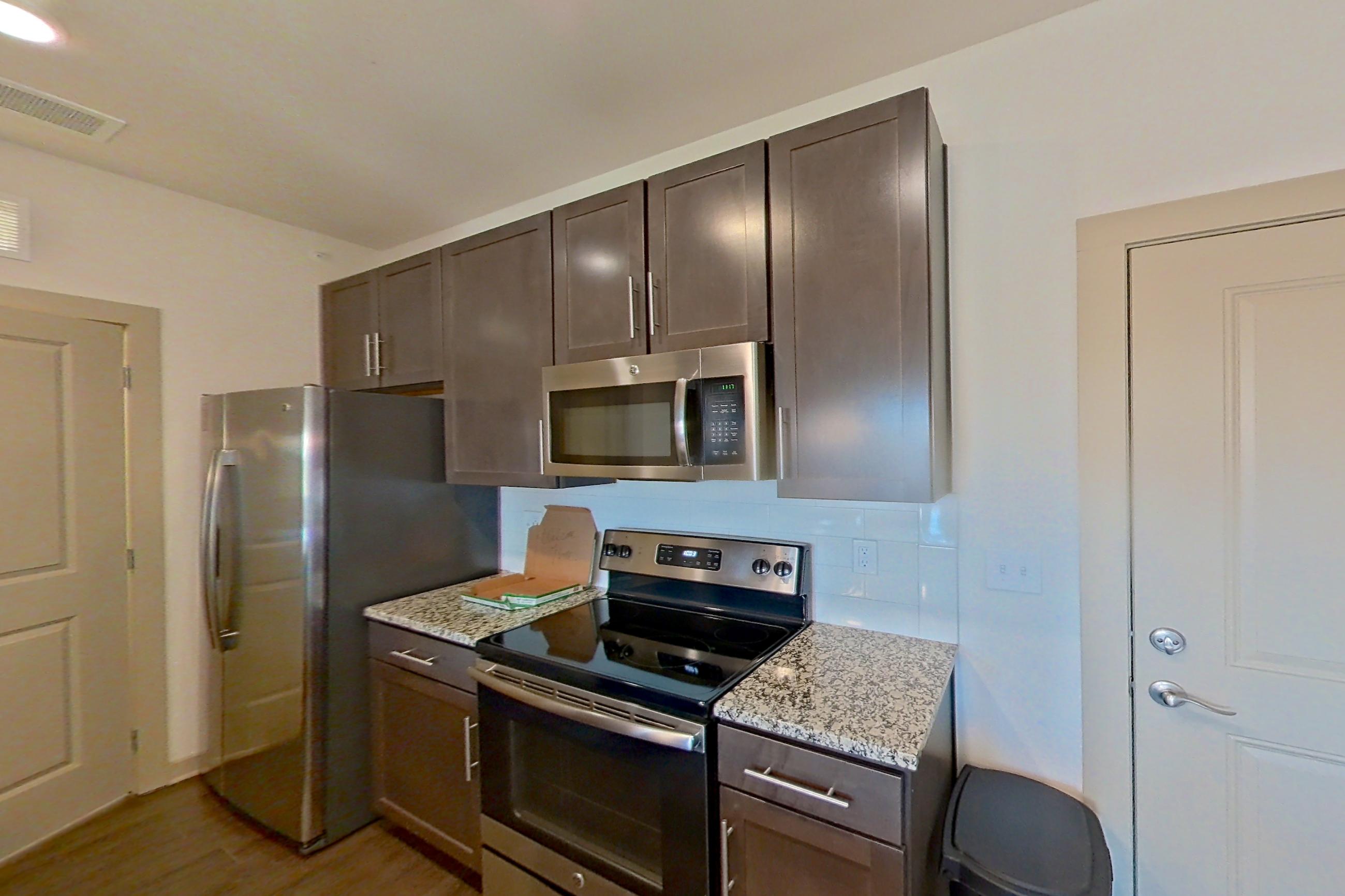 Kitchen with dark wood-finish flooring, dishwasher, electric range, light stone countertops, light wood-finish flooring, microwave, oven/range, refrigerator, and stainless steel appliances, Apartment 1-519 at Aventine Northshore