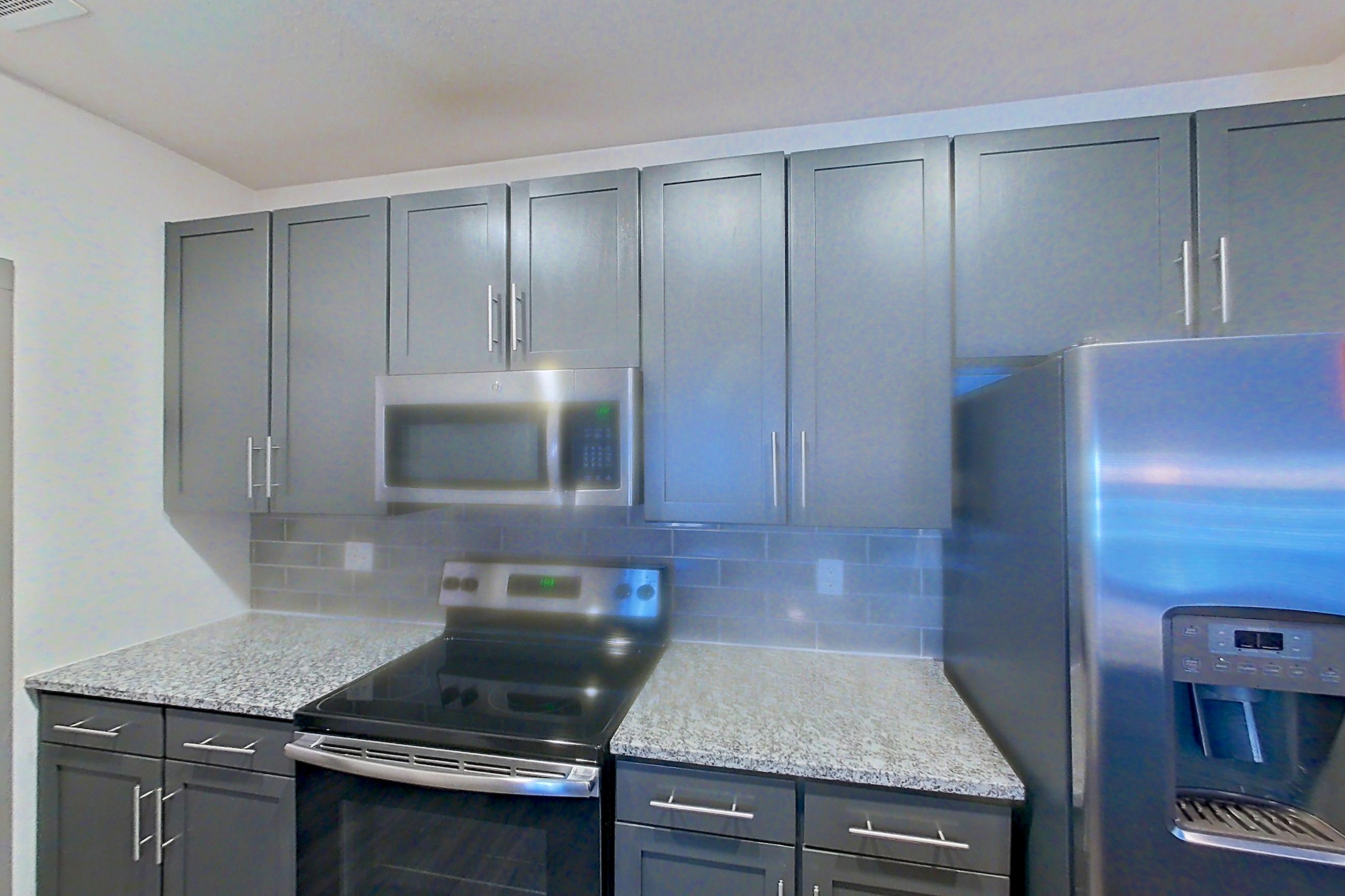 Kitchen with dark wood-finish flooring, electric range, light countertops, light stone countertops, light wood-finish flooring, oven/range, refrigerator, stainless steel appliances, and water & ice dispenser, Apartment 9-204 at Aventine Northshore