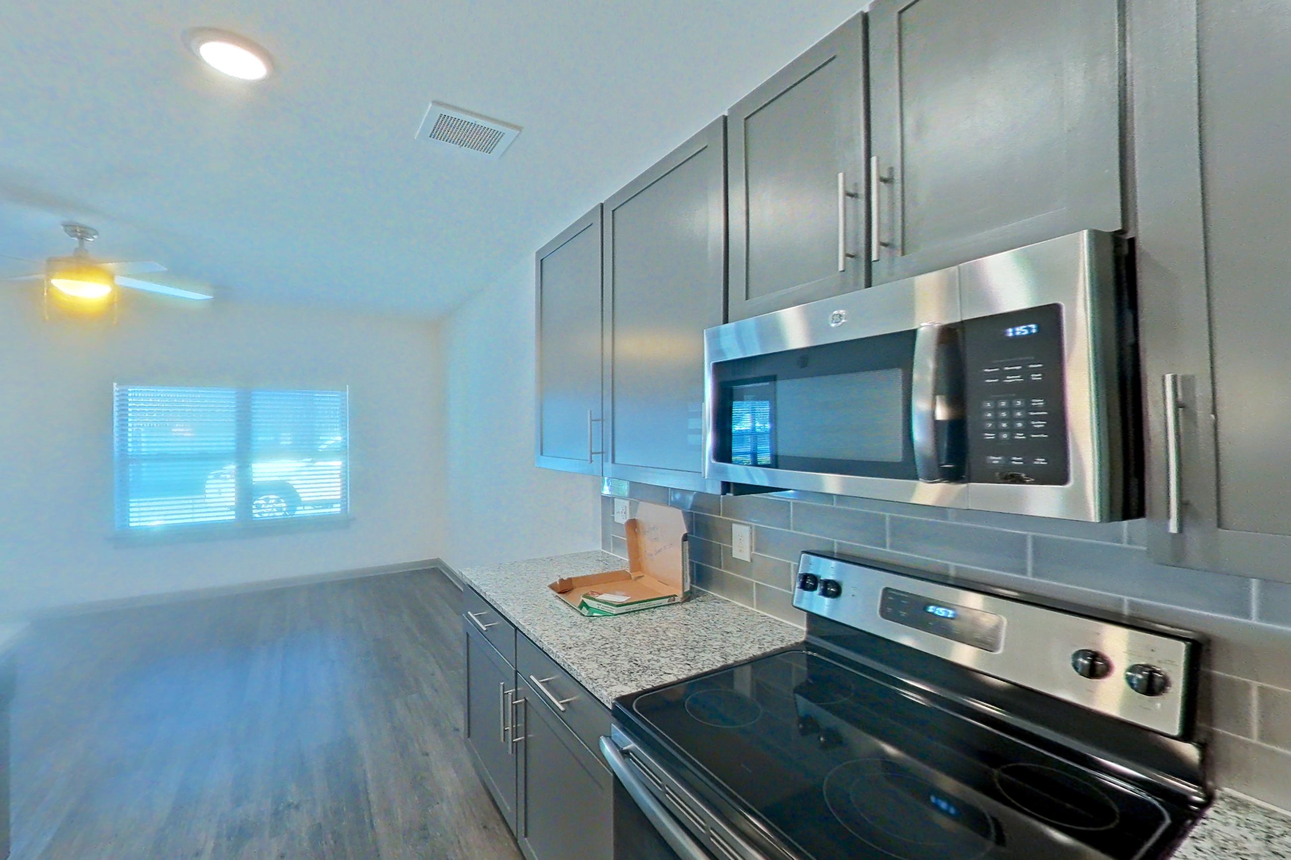 Kitchen with electric range, kitchen island, light stone countertops, light wood-finish flooring, microwave, oven/range, refrigerator, stainless steel appliances, and water & ice dispenser, Apartment 7-109 at Aventine Northshore
