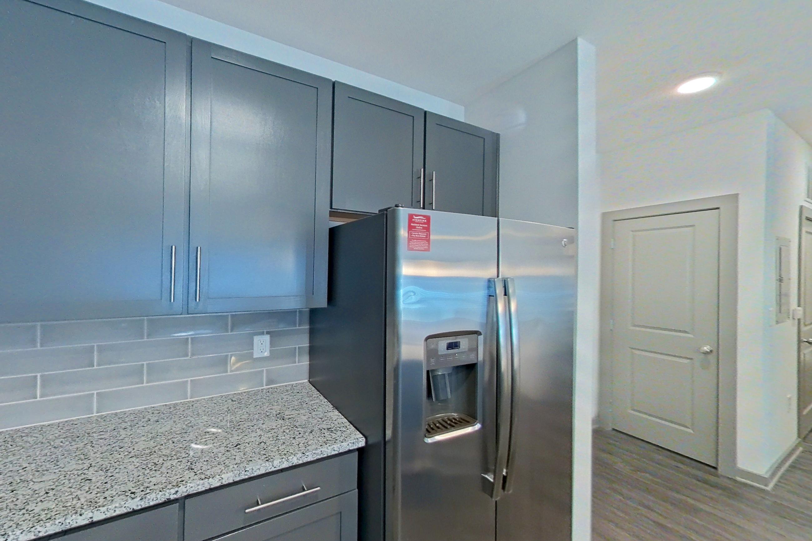 Kitchen with electric range, kitchen island, light stone countertops, light wood-finish flooring, microwave, oven/range, refrigerator, stainless steel appliances, and water & ice dispenser, Apartment 7-109 at Aventine Northshore
