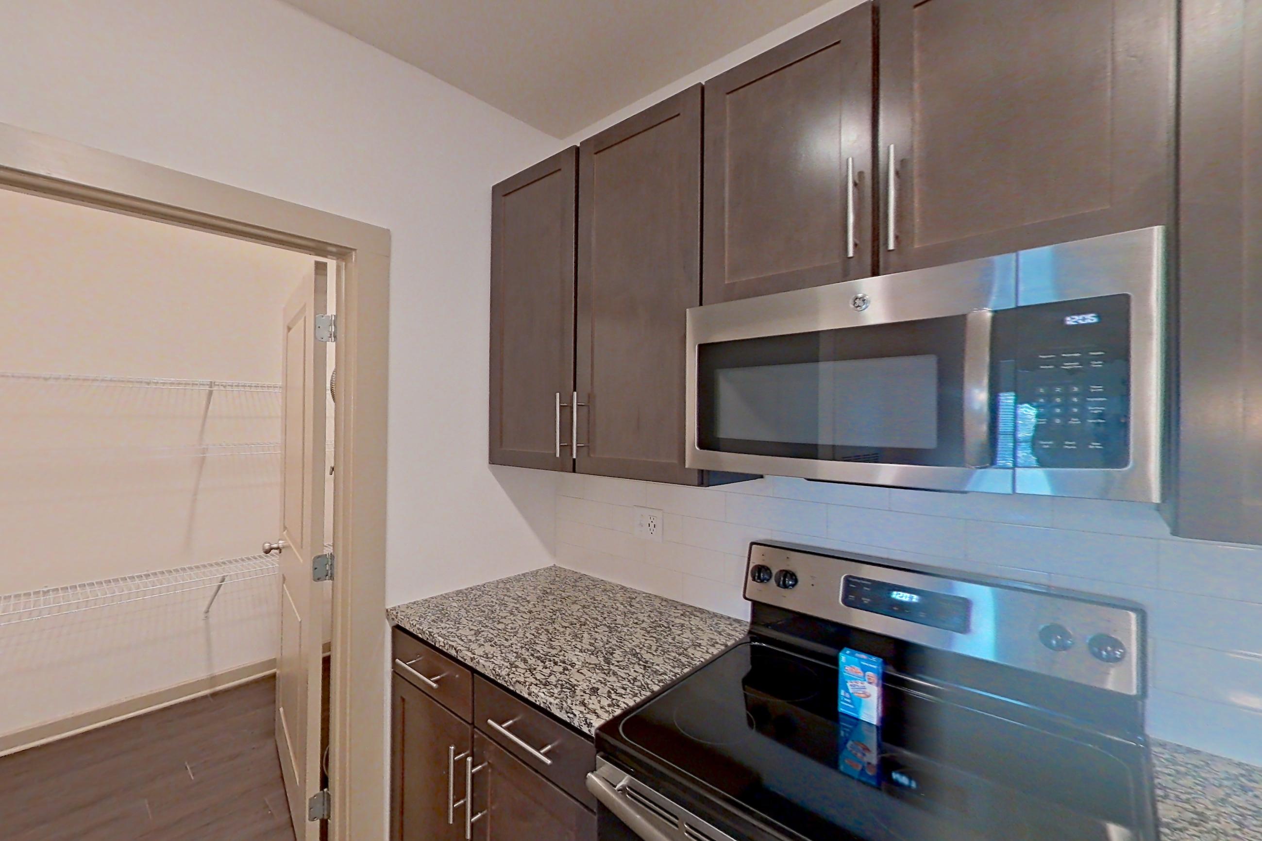 Kitchen with dark wood-finish flooring, electric range, kitchen island, light stone countertops, microwave, oven/range, refrigerator, and stainless steel appliances, Apartment 7-203 at Aventine Northshore